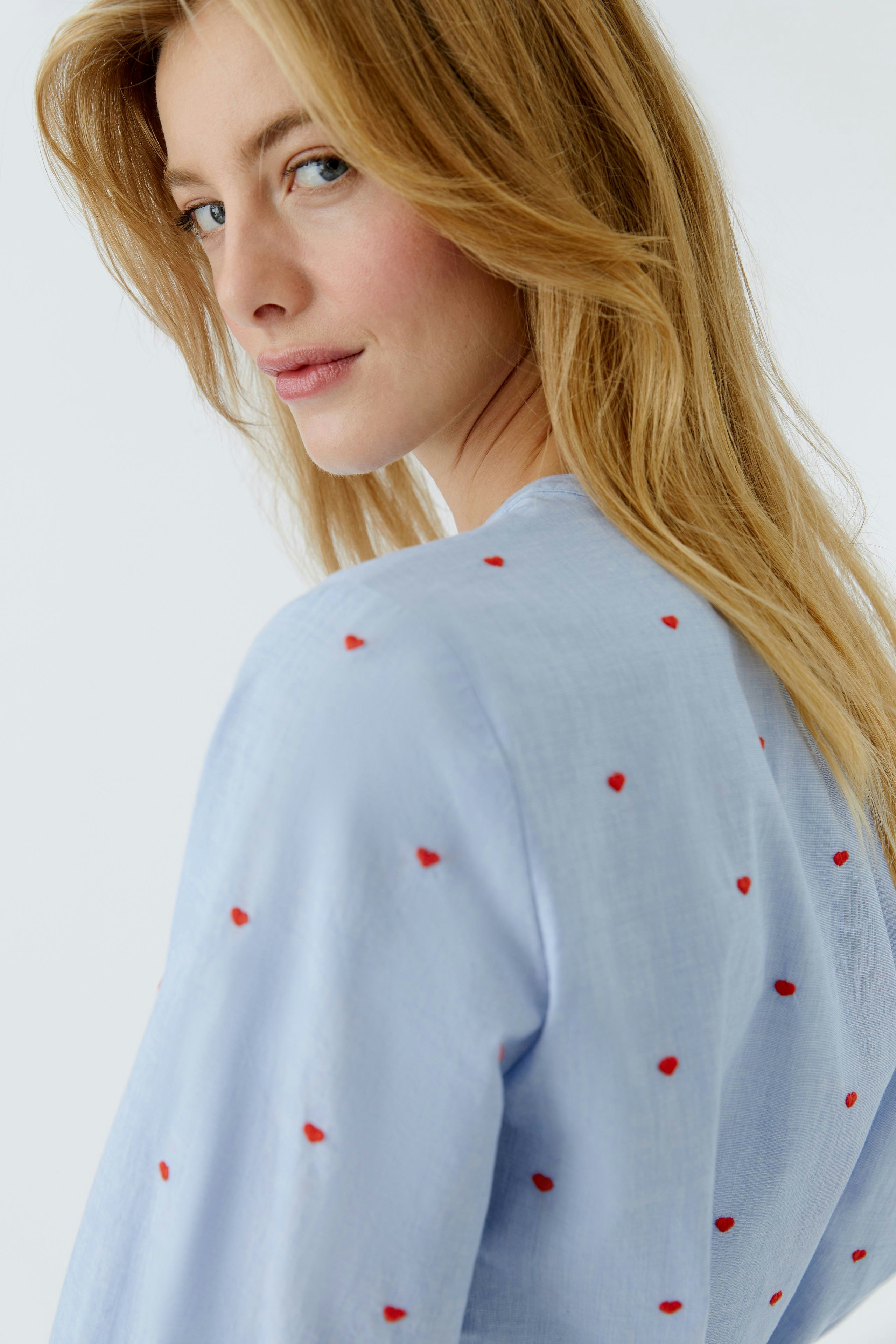 Light blue blouse with red heart embroidery, worn by a woman, showcasing a casual style.