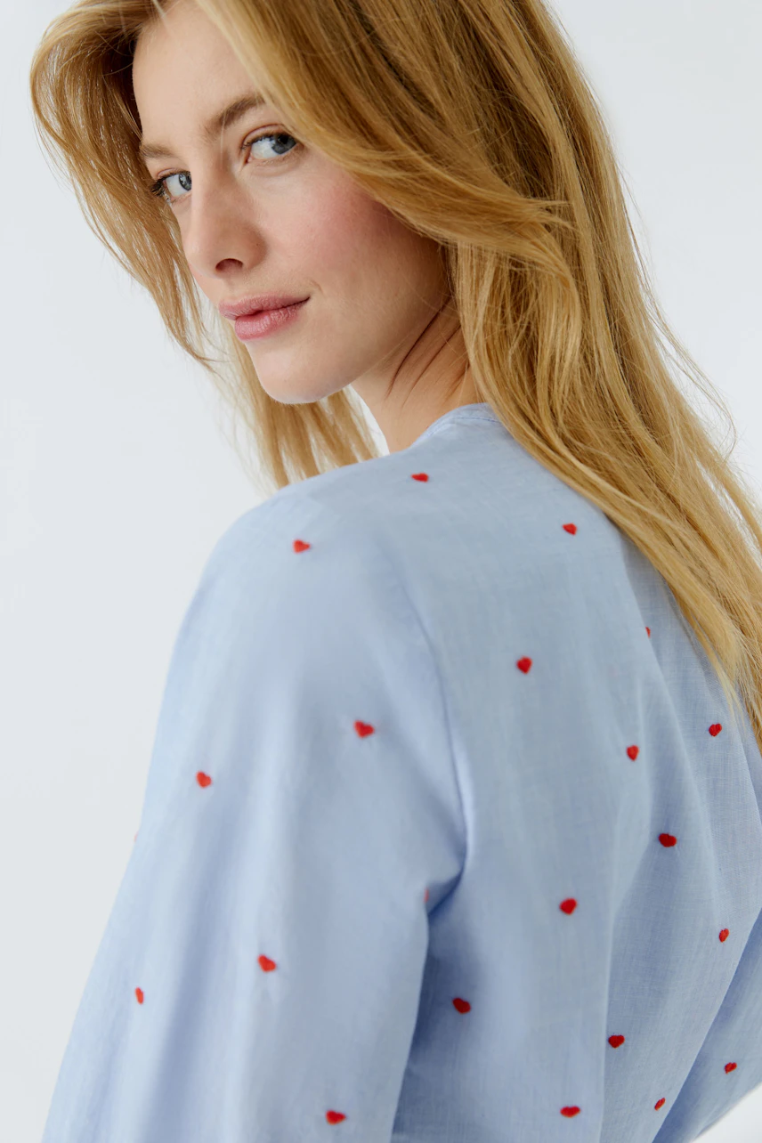 Light blue blouse with red heart embroidery, worn by a woman, showcasing a casual style.