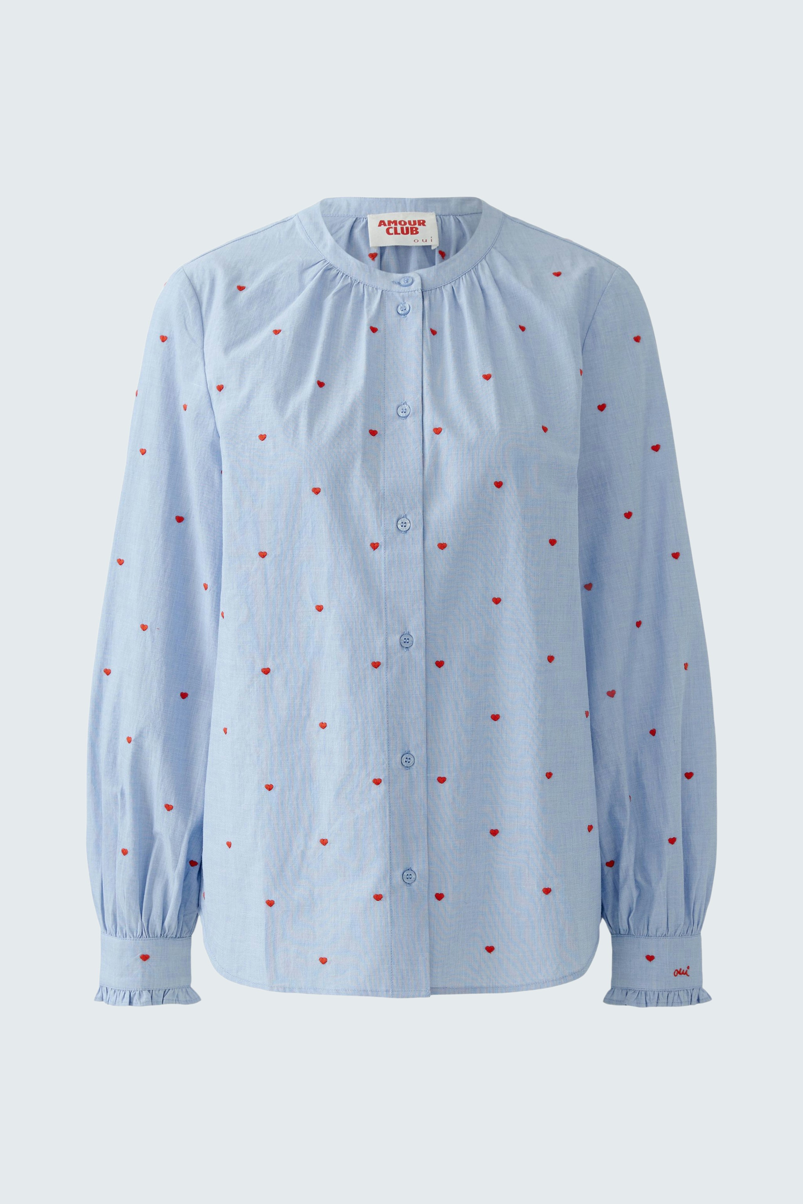 Light blue blouse with red dots, featuring a round neckline and long sleeves.
