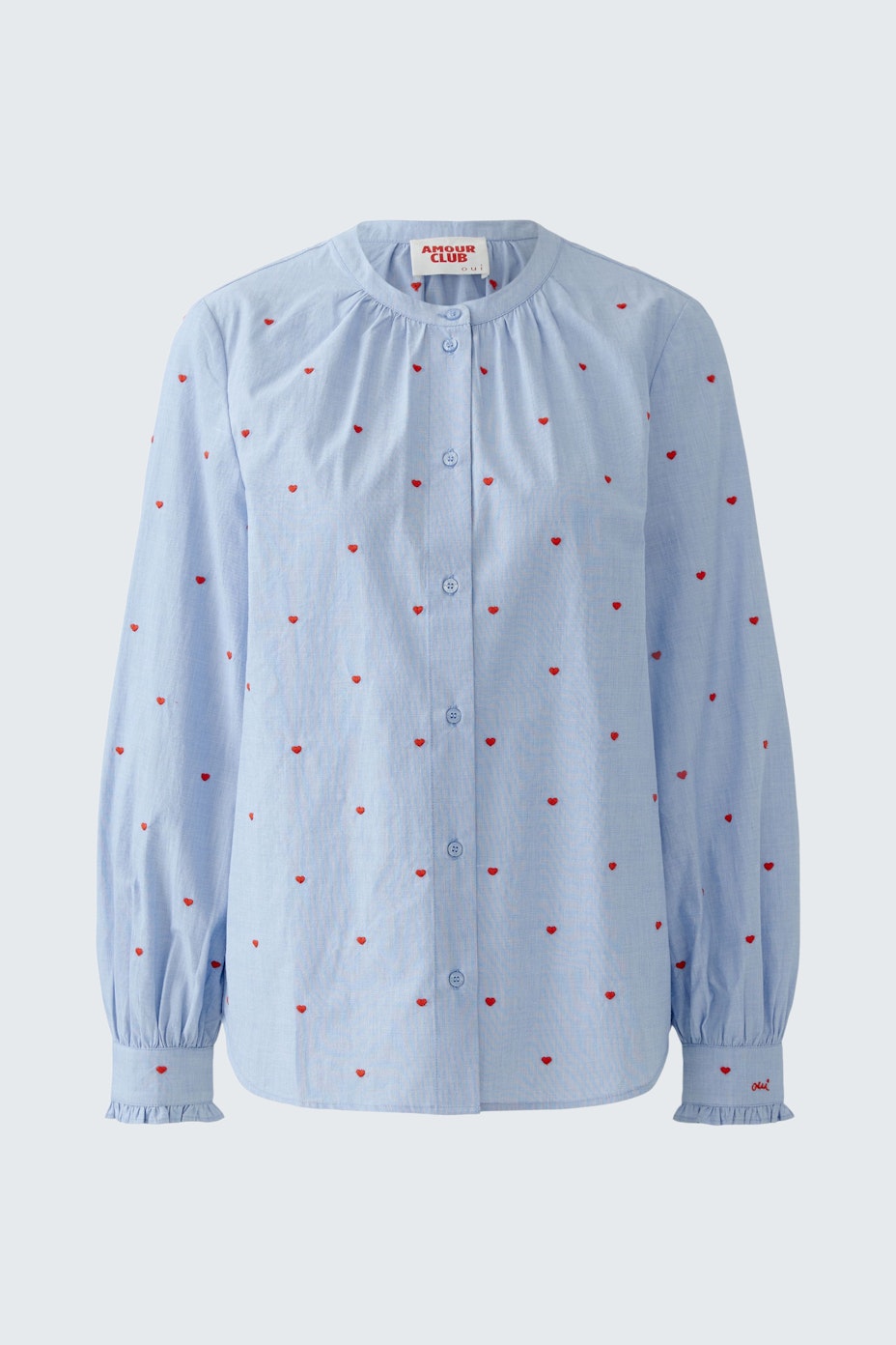 Light blue blouse with red dots, featuring a round neckline and long sleeves.