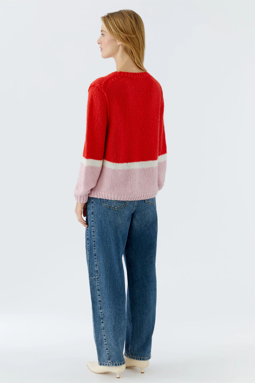 Casual women's pullover: Young woman in a red and pink color-blocked pullover with relaxed fit.