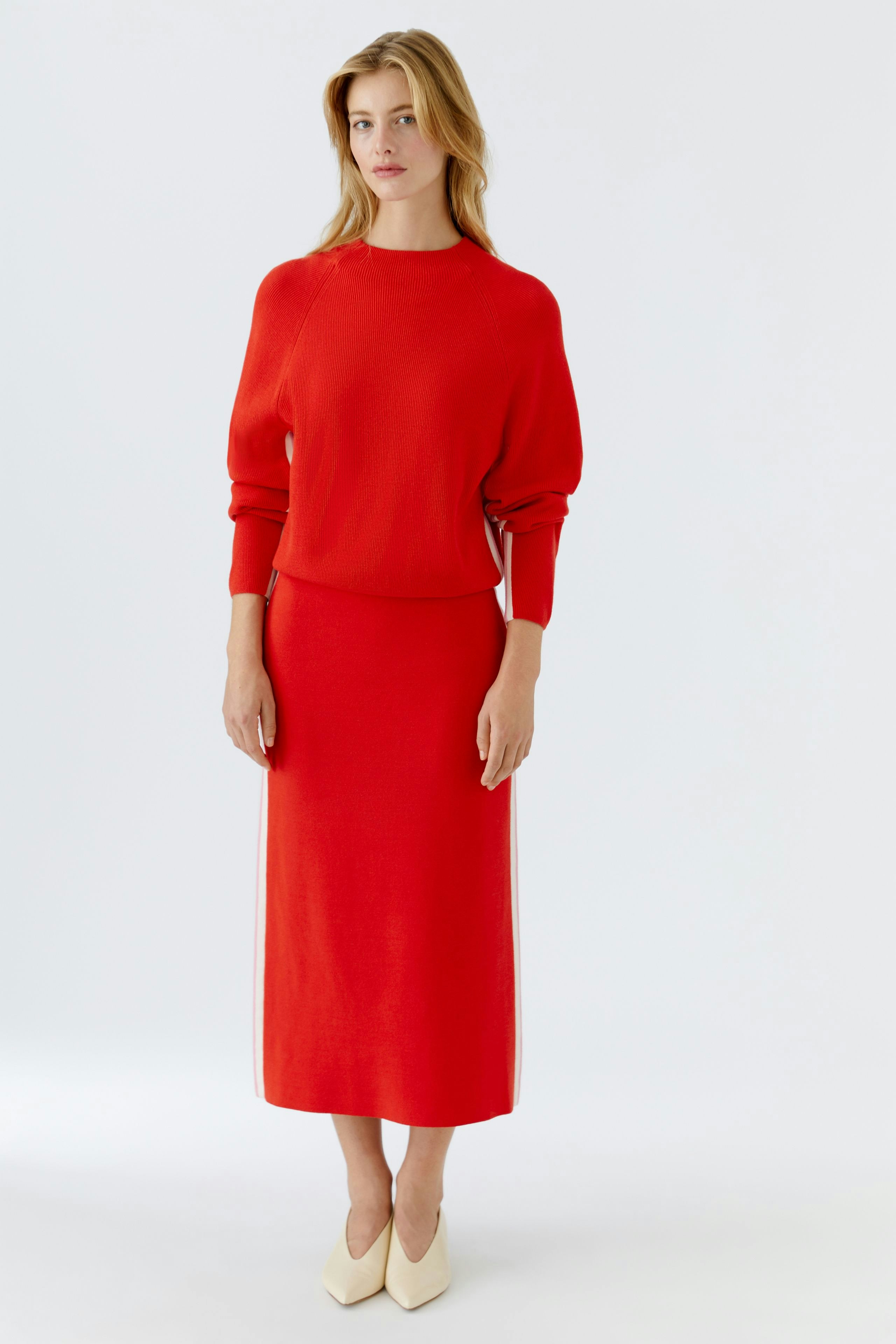 Modern women's pullover: A woman in a red pullover paired with a matching skirt, showcasing a relaxed style.