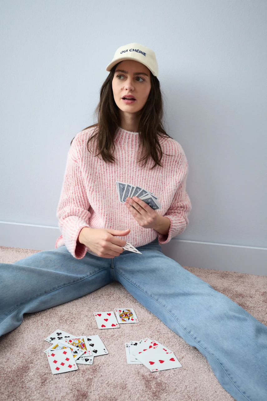 Casual women's pullover: Young woman in a pink knitted pullover, playing cards on the floor.