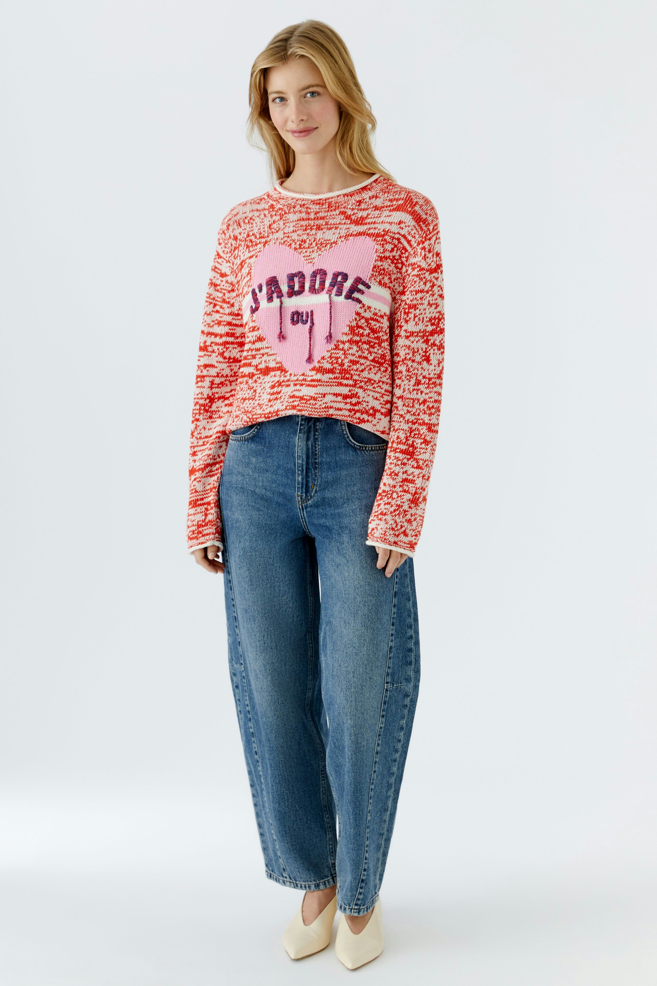 Damen-Pullover in Rot mit Herz-Motiv und lässigem Schnitt, kombiniert mit Jeans und Schuhen.