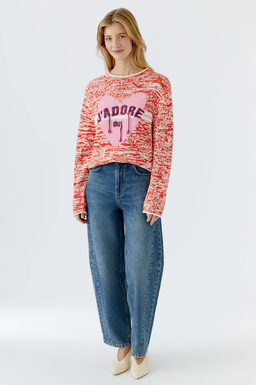Casual women's pullover: Young woman in a red knit pullover with a heart design and relaxed jeans.