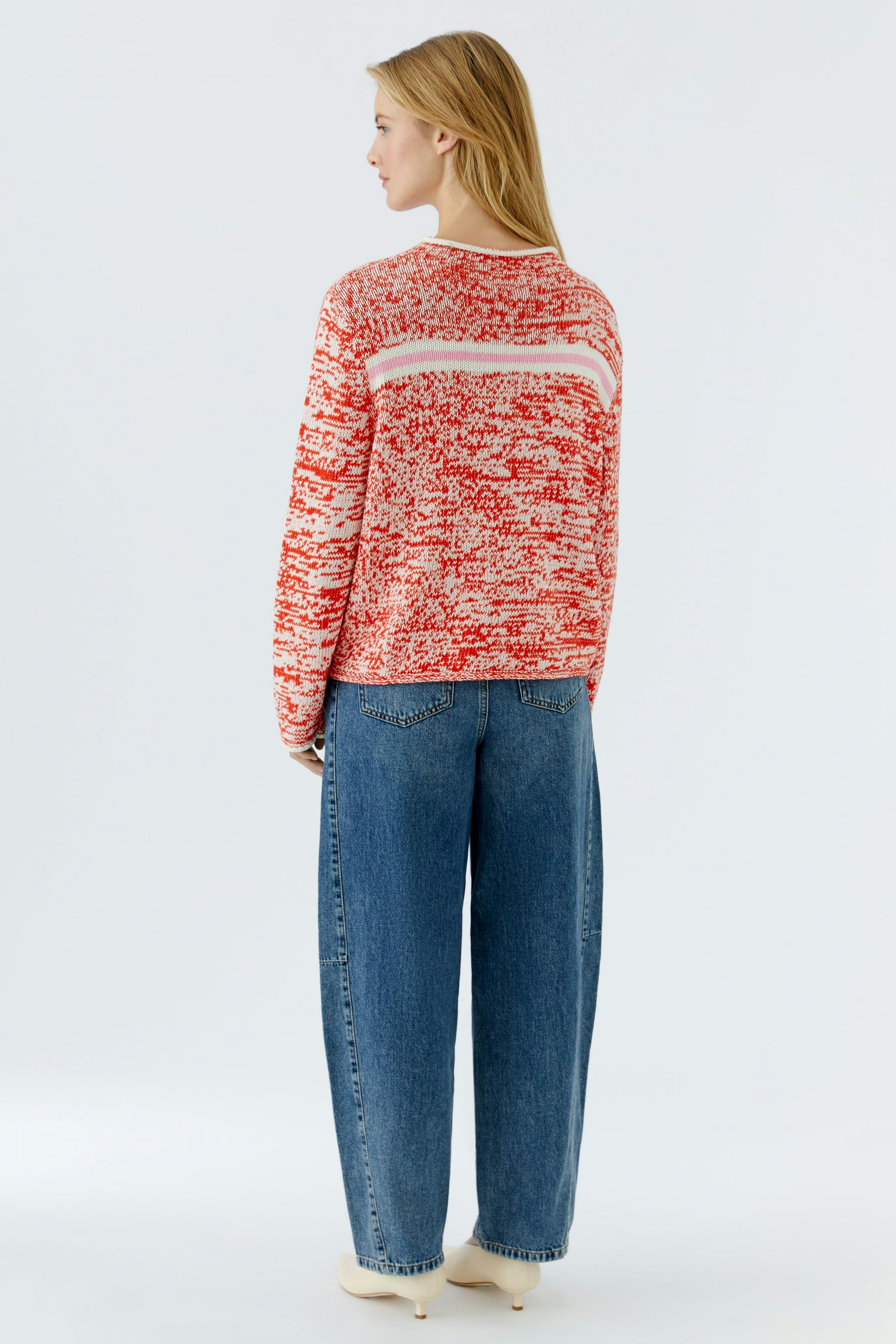 Damen-Pullover: Frau trägt einen rot-weißen Strickpullover mit lässigem Schnitt und weiten Jeans.