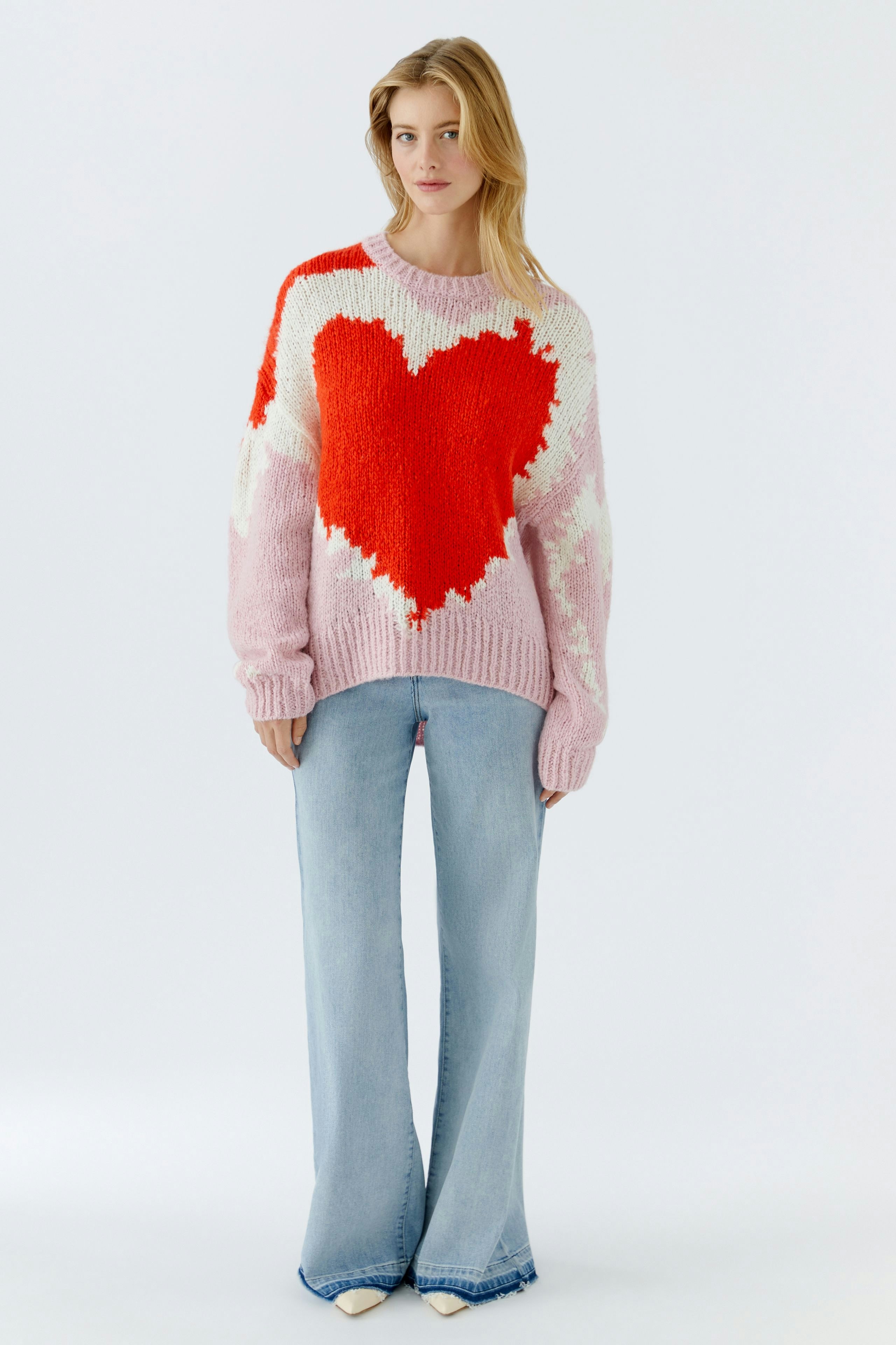 Bunter Damen-Pullover: Frau trägt einen rosa Pullover mit rotem Herzmotiv und lässigen Jeans.