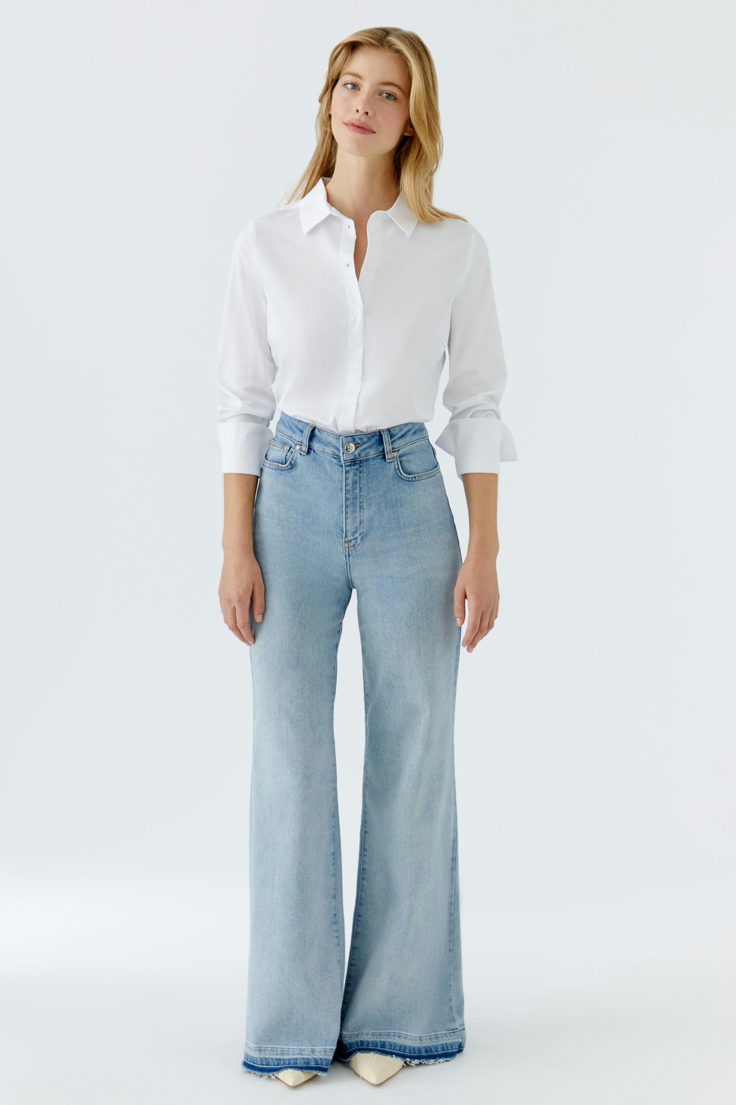 Flared jeans: Woman in light blue flared jeans paired with a white shirt, showcasing a casual style.