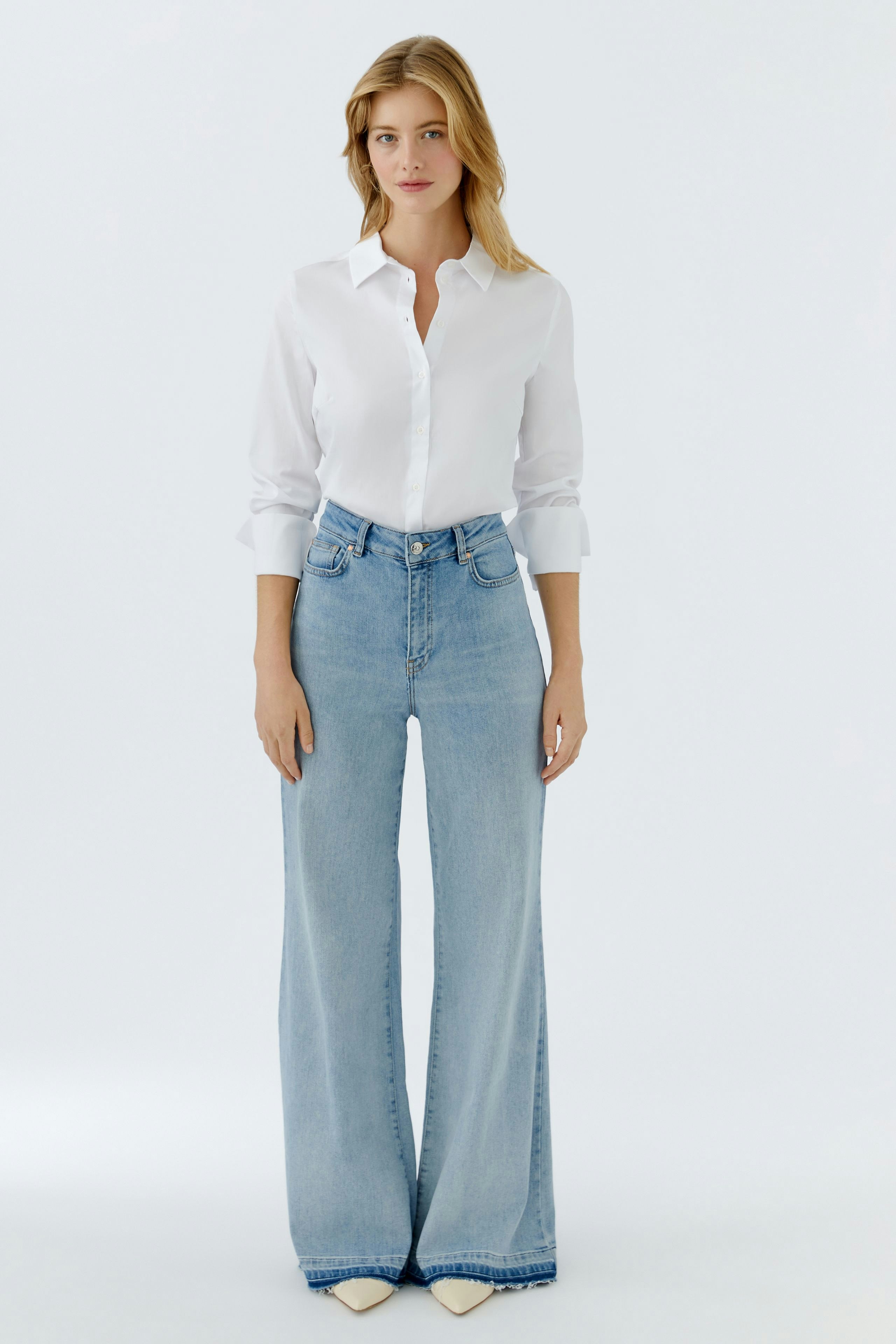 Flared jeans: Woman in light blue flared jeans paired with a white shirt, showcasing a casual style.
