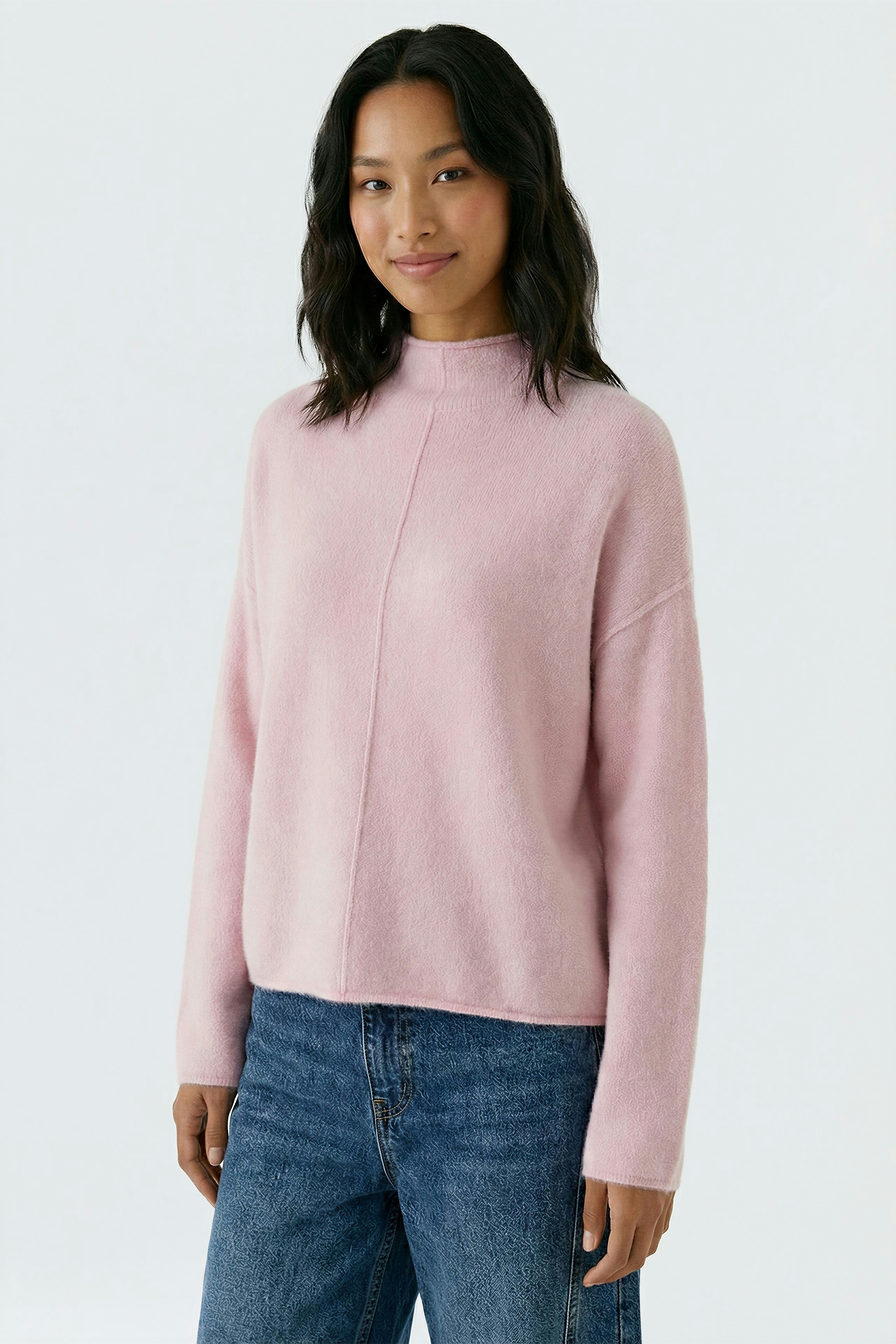 Damen-Pullover: Frau in rosa Strickpullover mit hohem Kragen und lässigen Jeans lächelt freundlich.