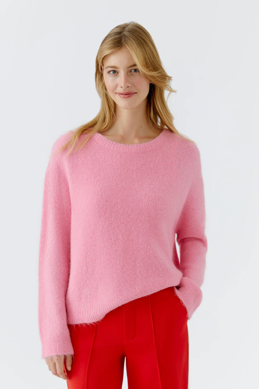 Casual women's pullover: A woman in a soft pink pullover paired with red pants smiles confidently.