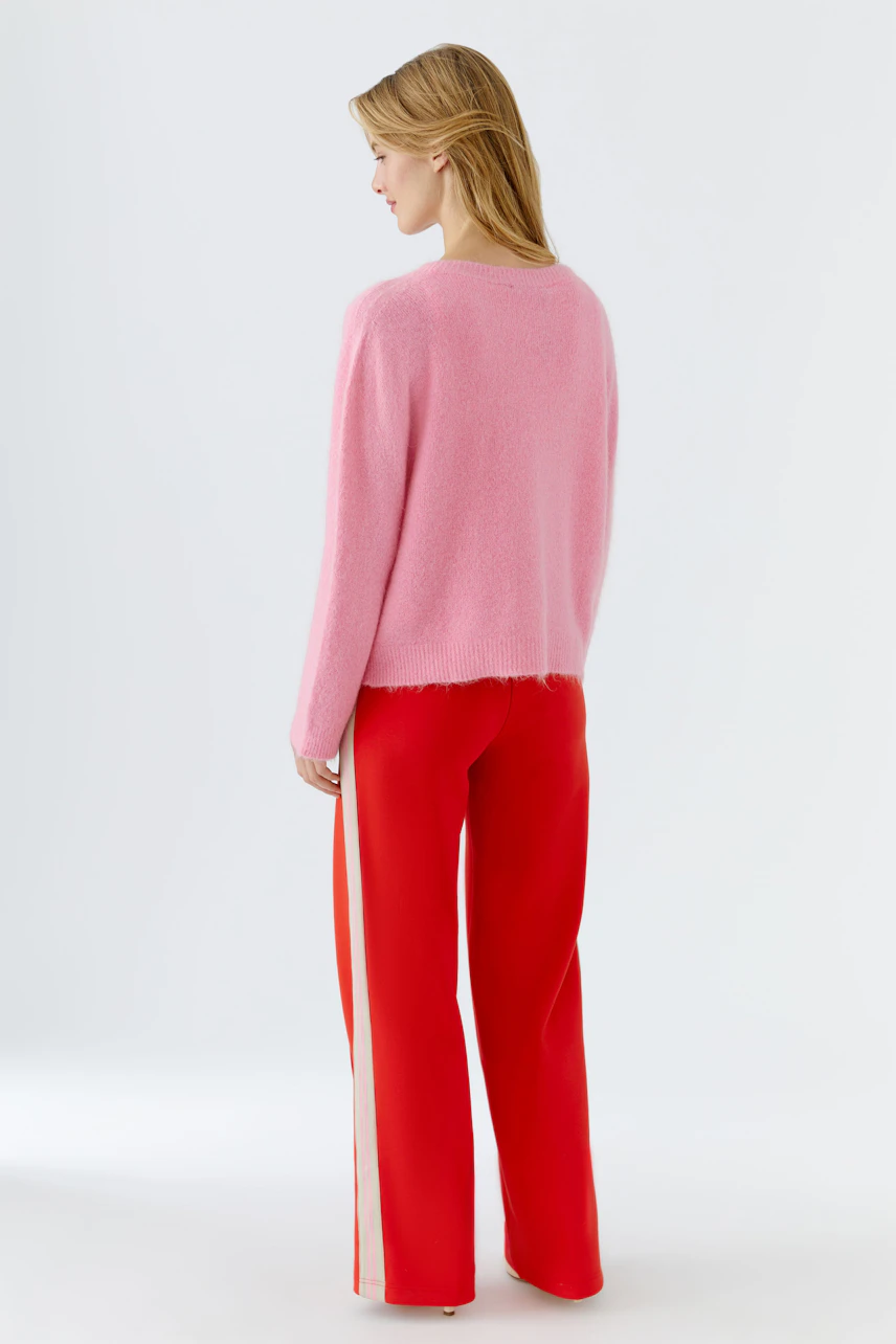 Casual women's pullover: A woman in a soft pink pullover paired with red pants, showcasing a relaxed style.