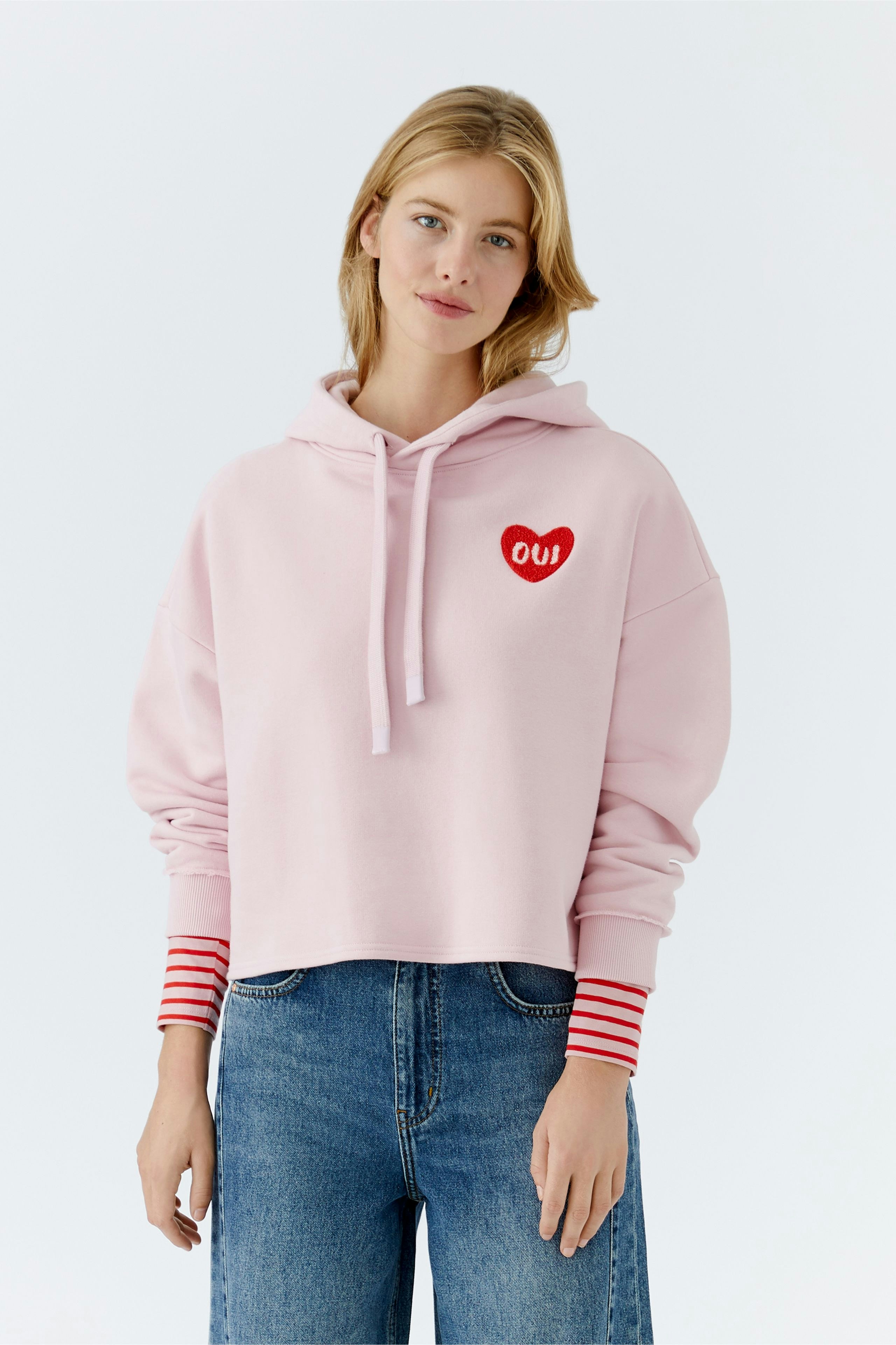 Bequemer Damen-Hoodie: Frau in rosa Kapuzenpullover mit Herz-Logo und gestreiften Ärmeln.
