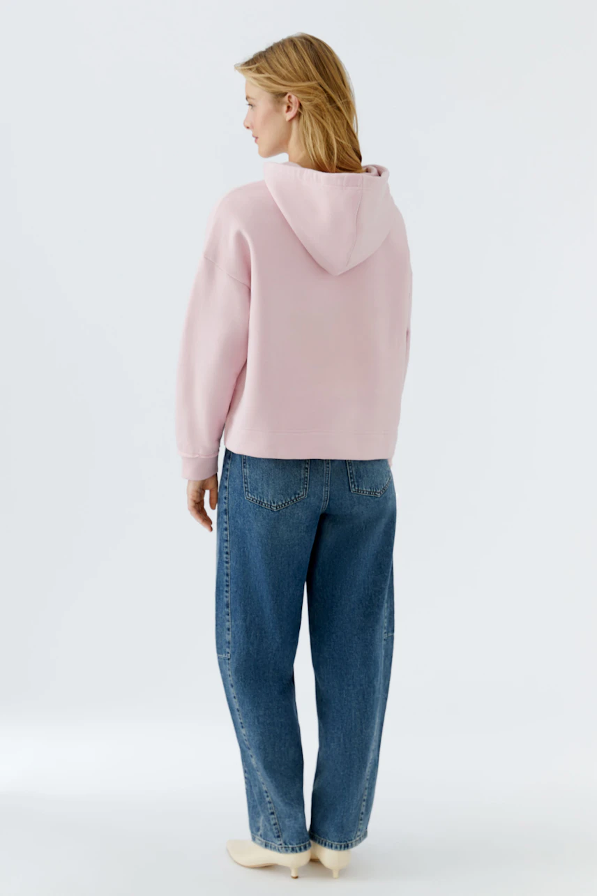 Casual women's hoodie: Young woman in a pink pullover with a hood, paired with relaxed-fit jeans.