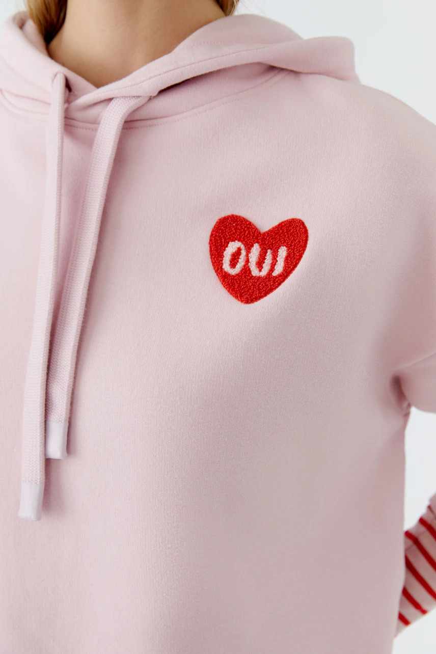 Casual women's hoodie in soft pink with a red heart logo, perfect for relaxed outfits.