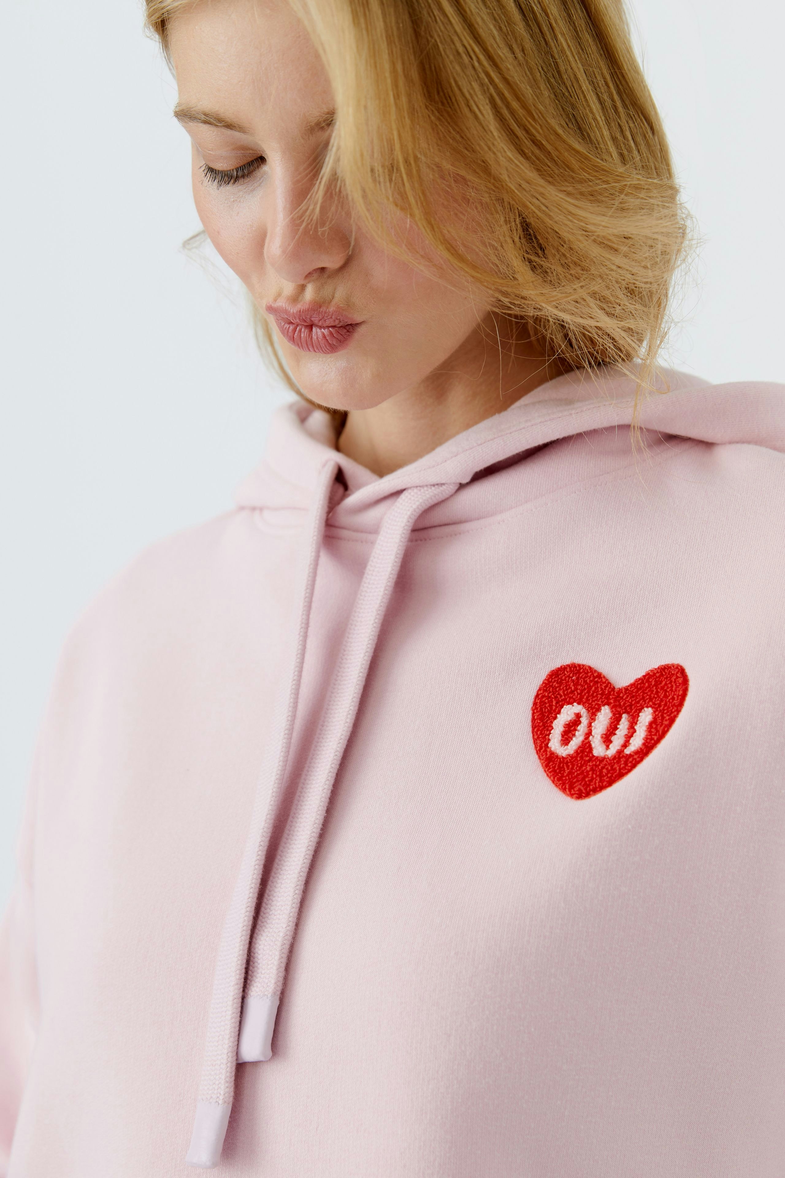 Bequemer Damen-Hoodie in zartem Rosa mit rotem Herz-Logo. Ideal für lässige Outfits.