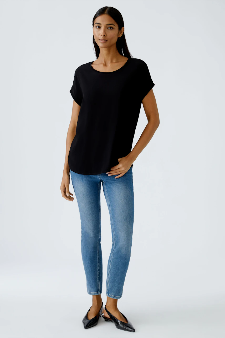 Schwarzes Blusenshirt: Frau trägt ein lässiges, lockeres Shirt mit kurzen Ärmeln und Jeans.