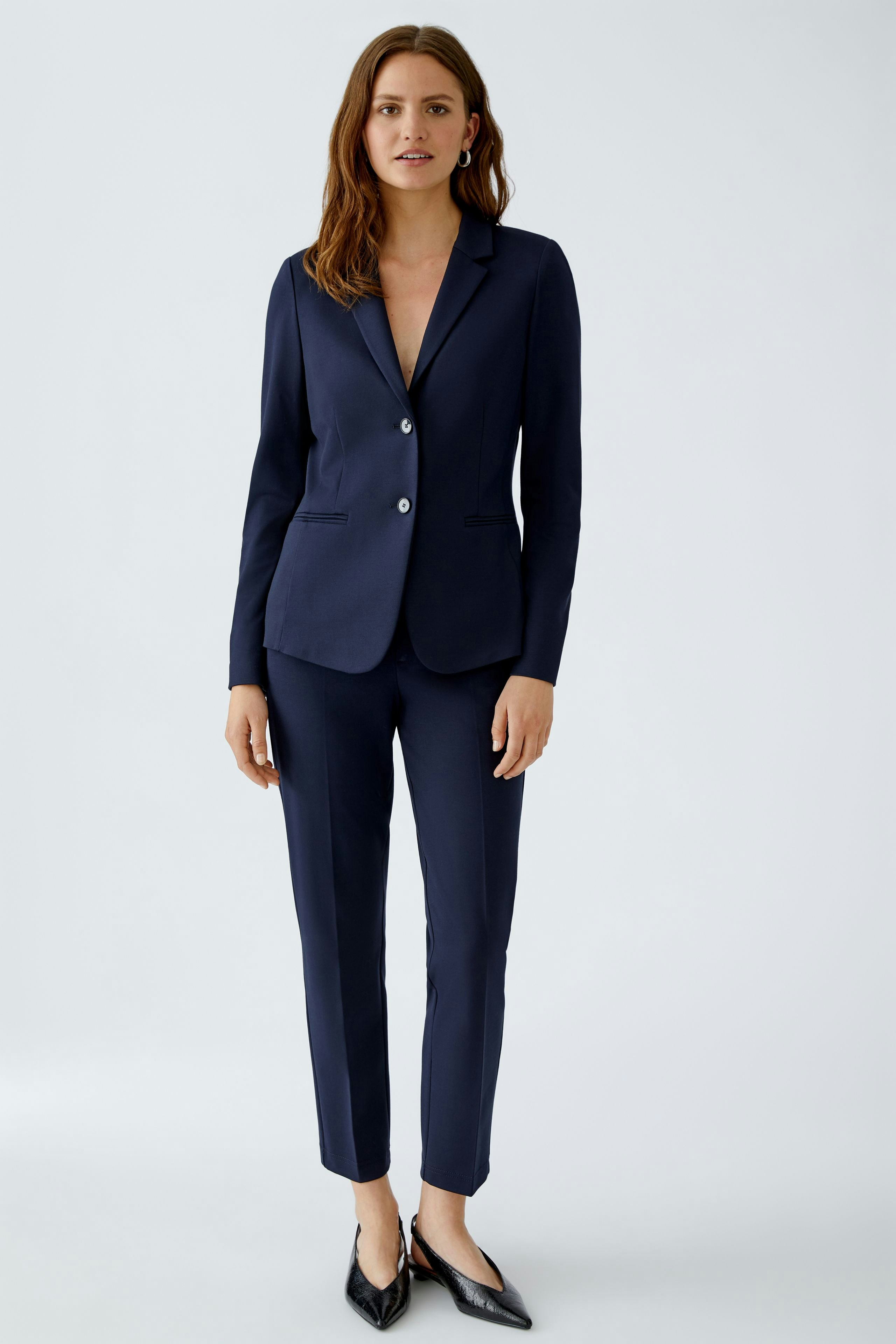 Moderne Damen-Hose: Frau in navyfarbener Hose und Blazer steht selbstbewusst vor neutralem Hintergrund.