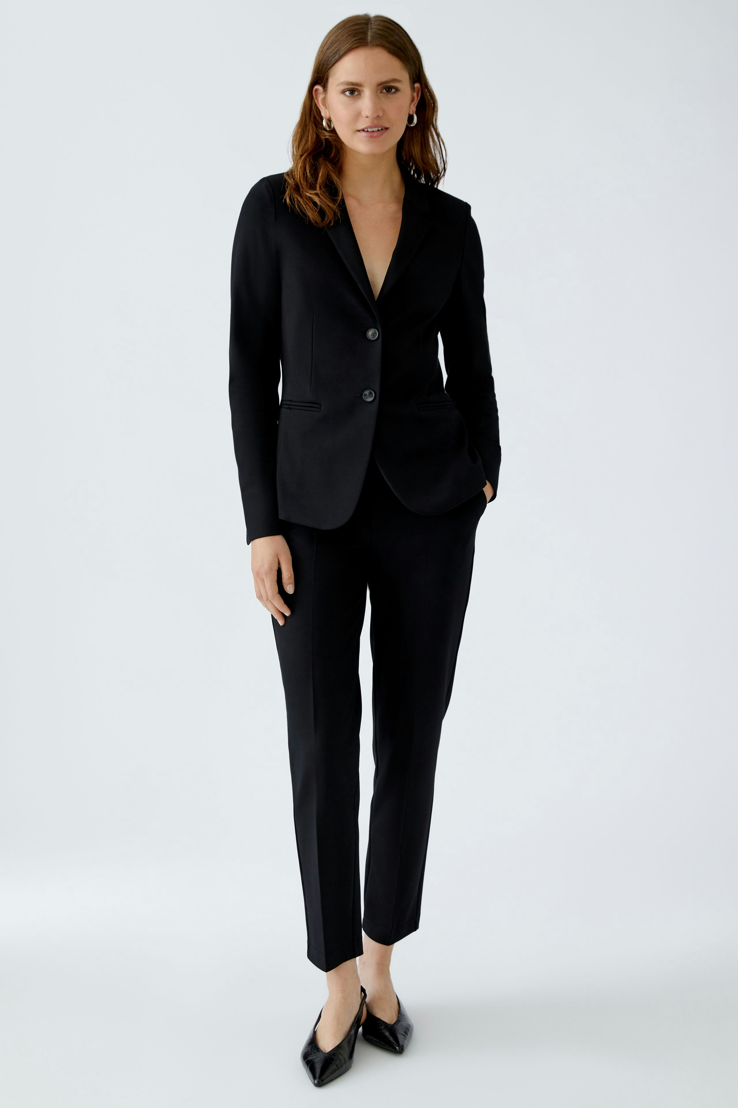 Chic women's trousers: A woman in tailored black trousers and a fitted blazer stands confidently.