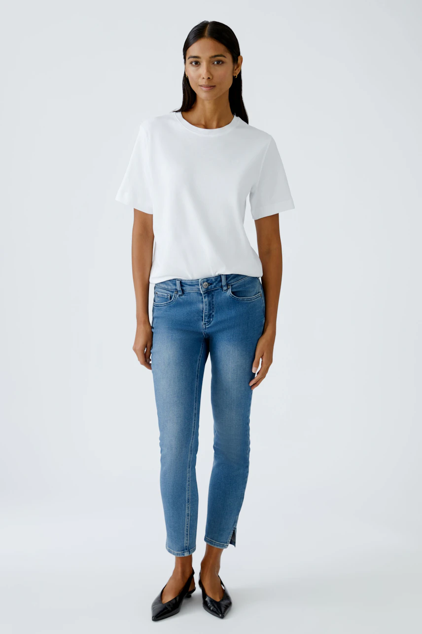 Damen Jeans Skinny: Frau in blauen Skinny Jeans und weißem T-Shirt steht lässig und selbstbewusst.