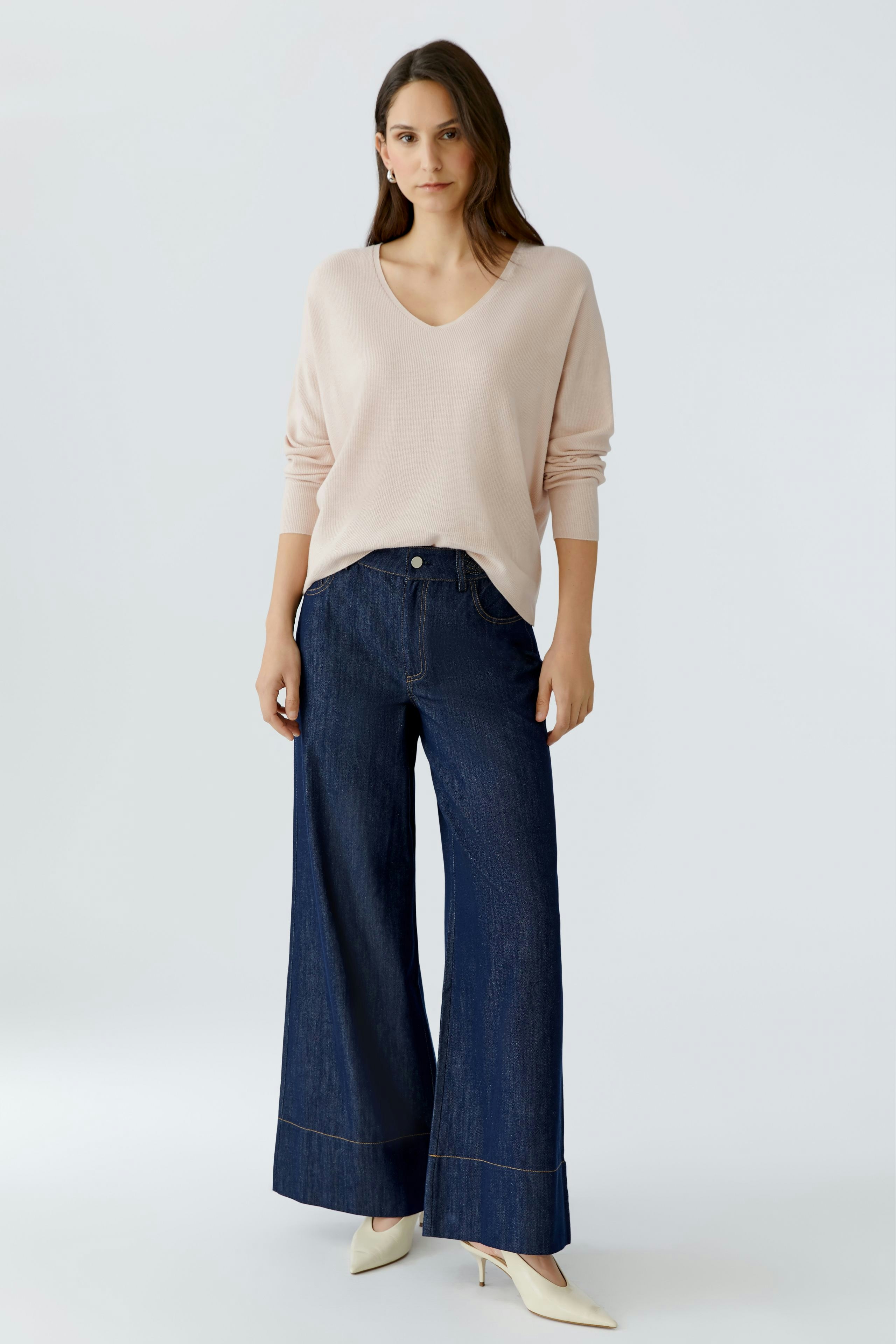 Damen-Pullover in zartem Rosa: Frau trägt einen lässigen V-Ausschnitt-Pullover zu weiten Jeans.