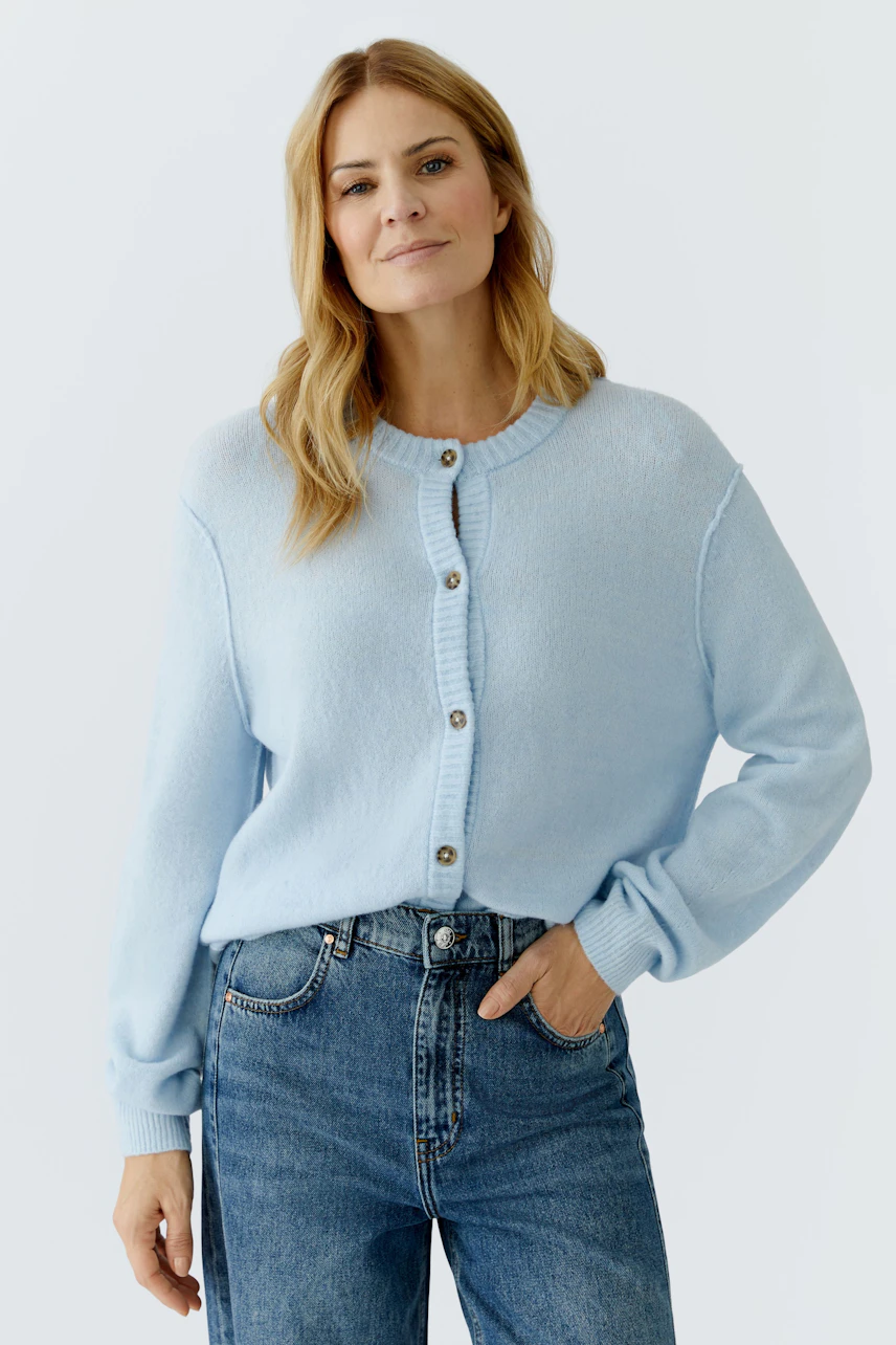 Casual women's cardigan: A woman in a light blue cardigan with buttons and relaxed jeans.