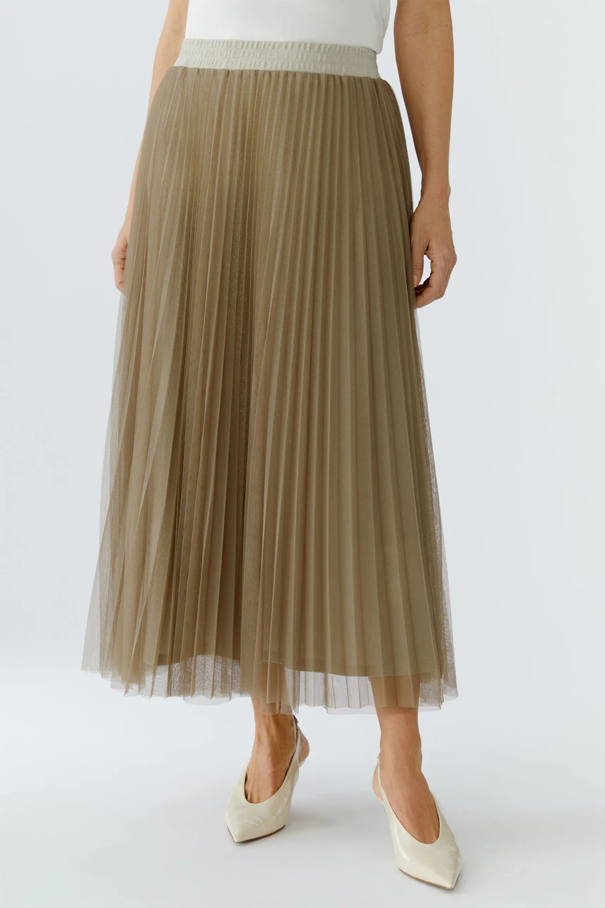 Pleated skirt: Woman in a flowy, beige pleated skirt paired with stylish heels.