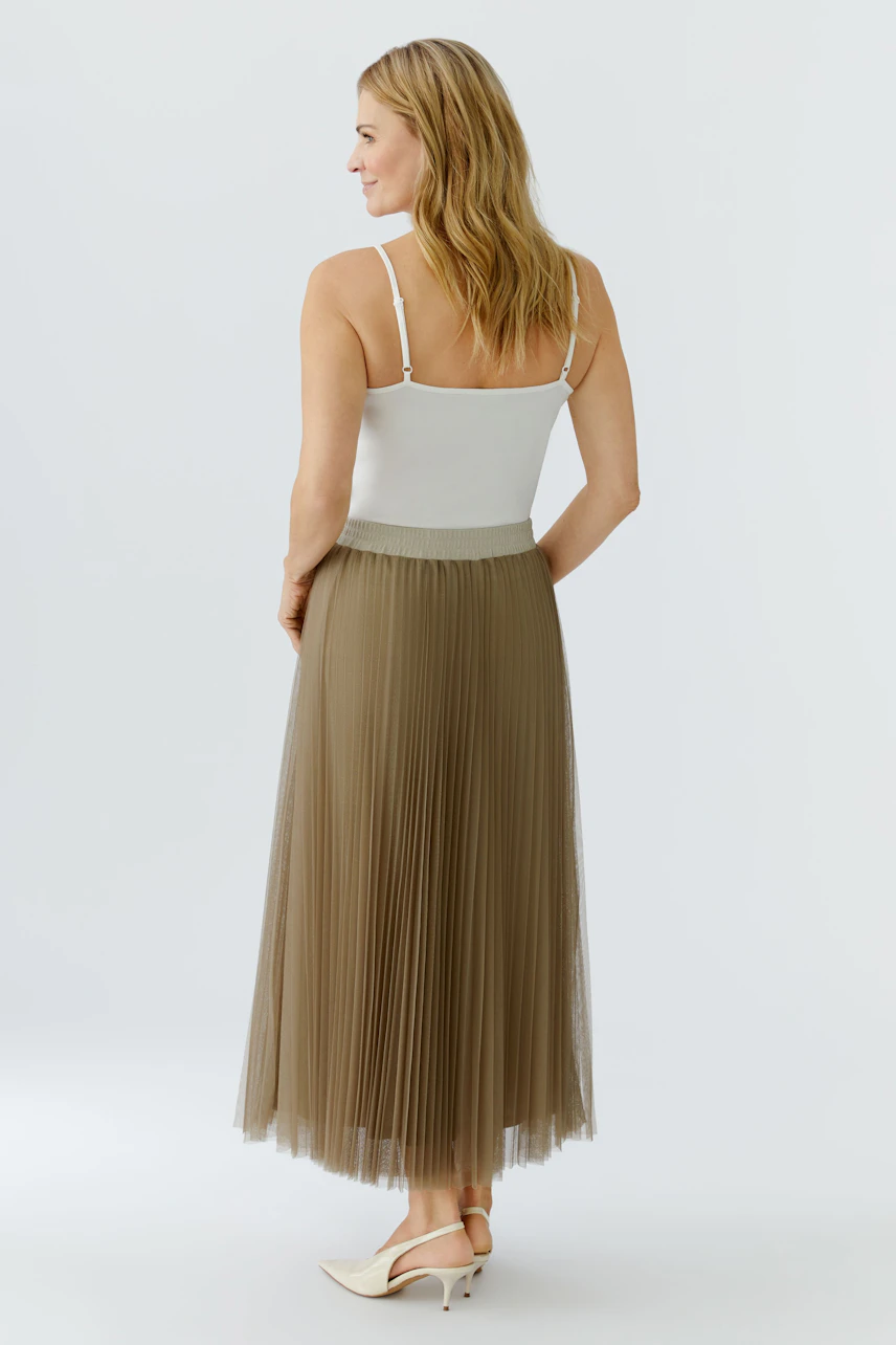 Pleated skirt: Woman in a light brown pleated skirt and white top, showcasing a casual style.