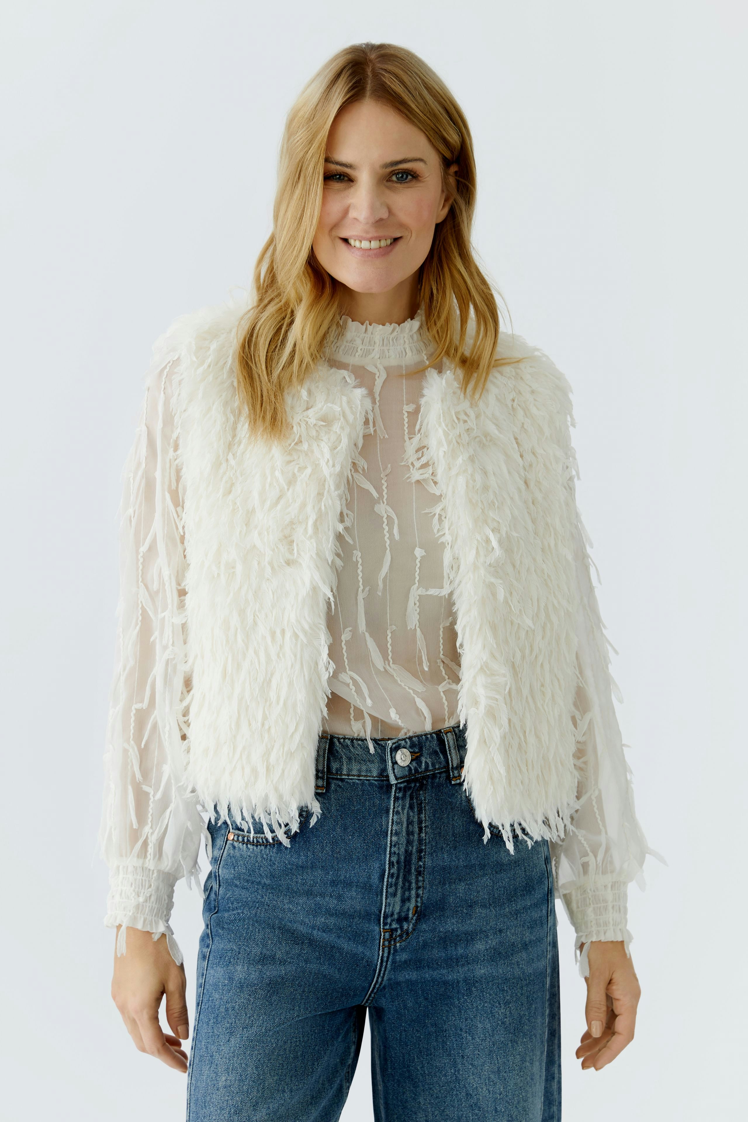 Fuzzy women's vest: A woman in a fluffy white vest over a sheer top and jeans, smiling confidently.