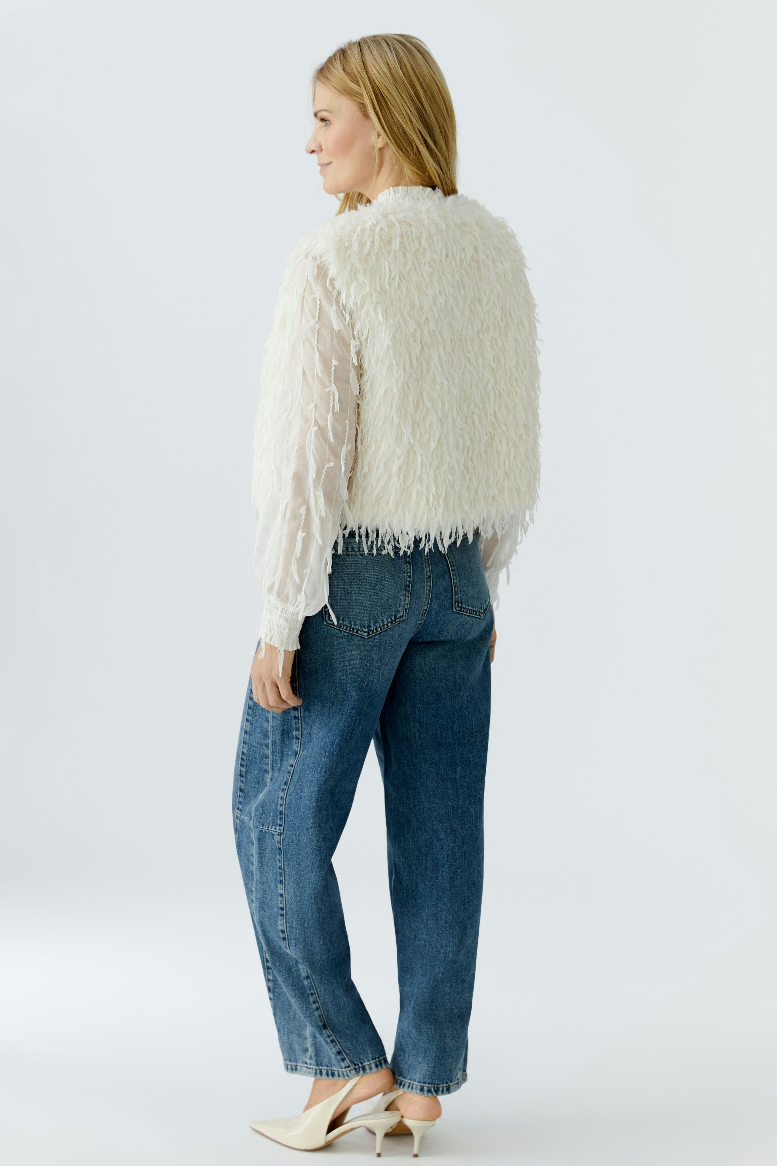 Cozy women's vest: A woman in a fluffy white vest over a sheer top and jeans, showcasing a casual look.