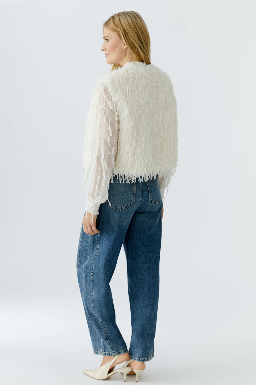 Cozy women's vest: A woman in a fluffy white vest over a sheer top and jeans, showcasing a casual look.