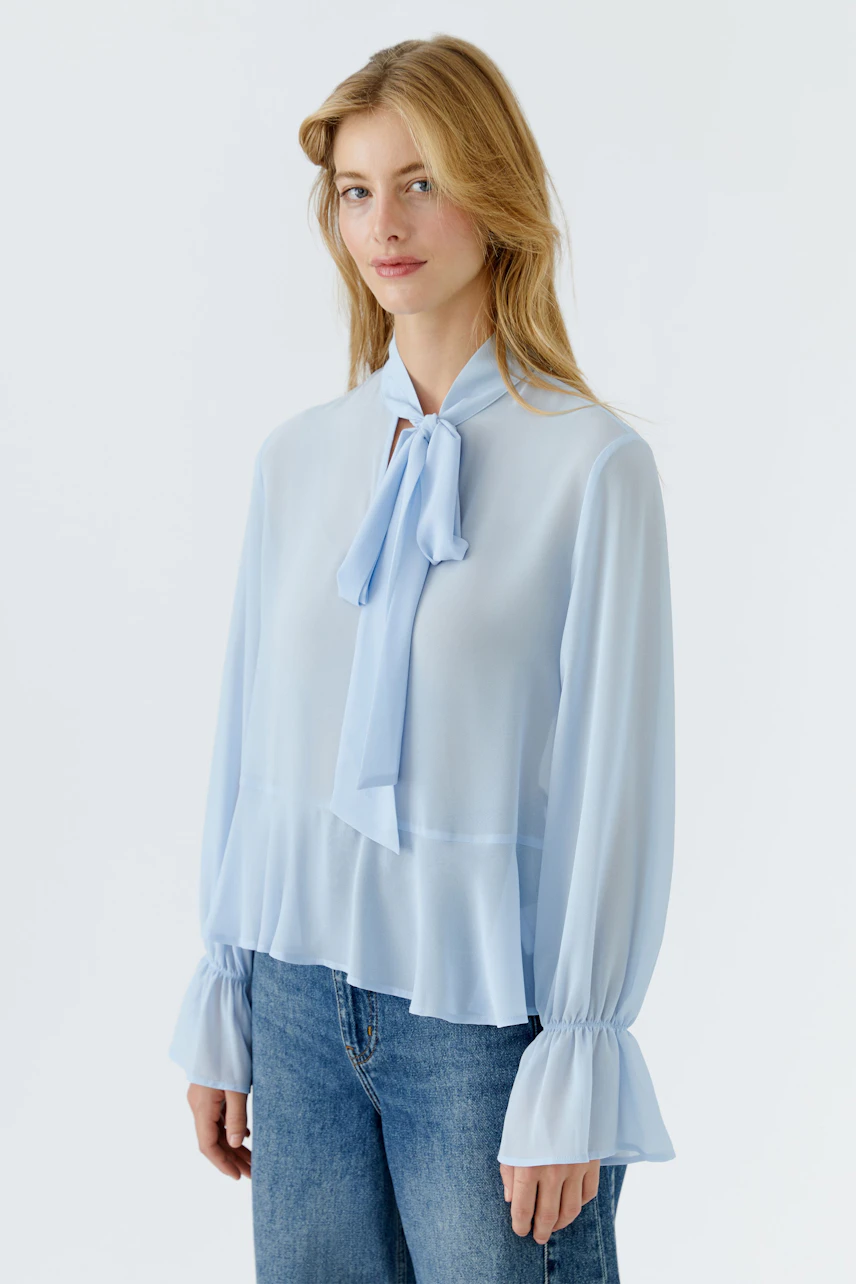 Helle Damen-Bluse mit Schleifenkragen und weiten Ärmeln, kombiniert mit lässigen Jeans.