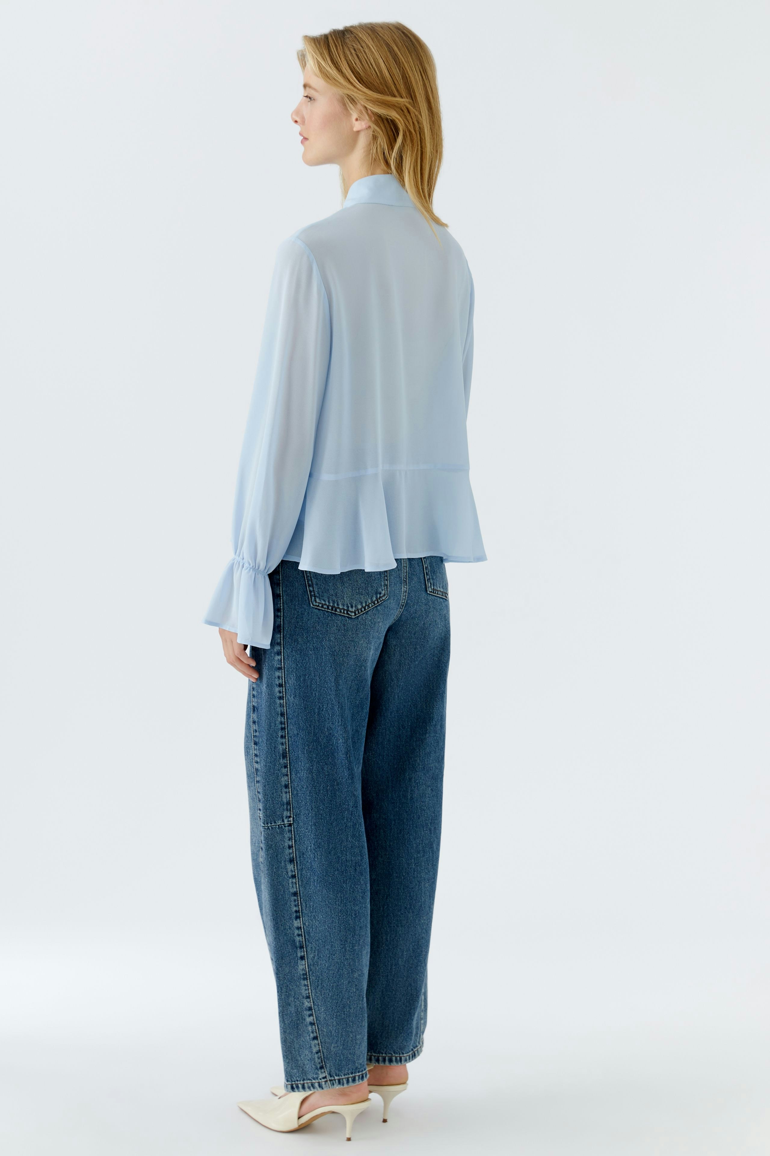 Light blue blouse: Woman in a flowing blouse with wide sleeves and relaxed jeans, viewed from the back.