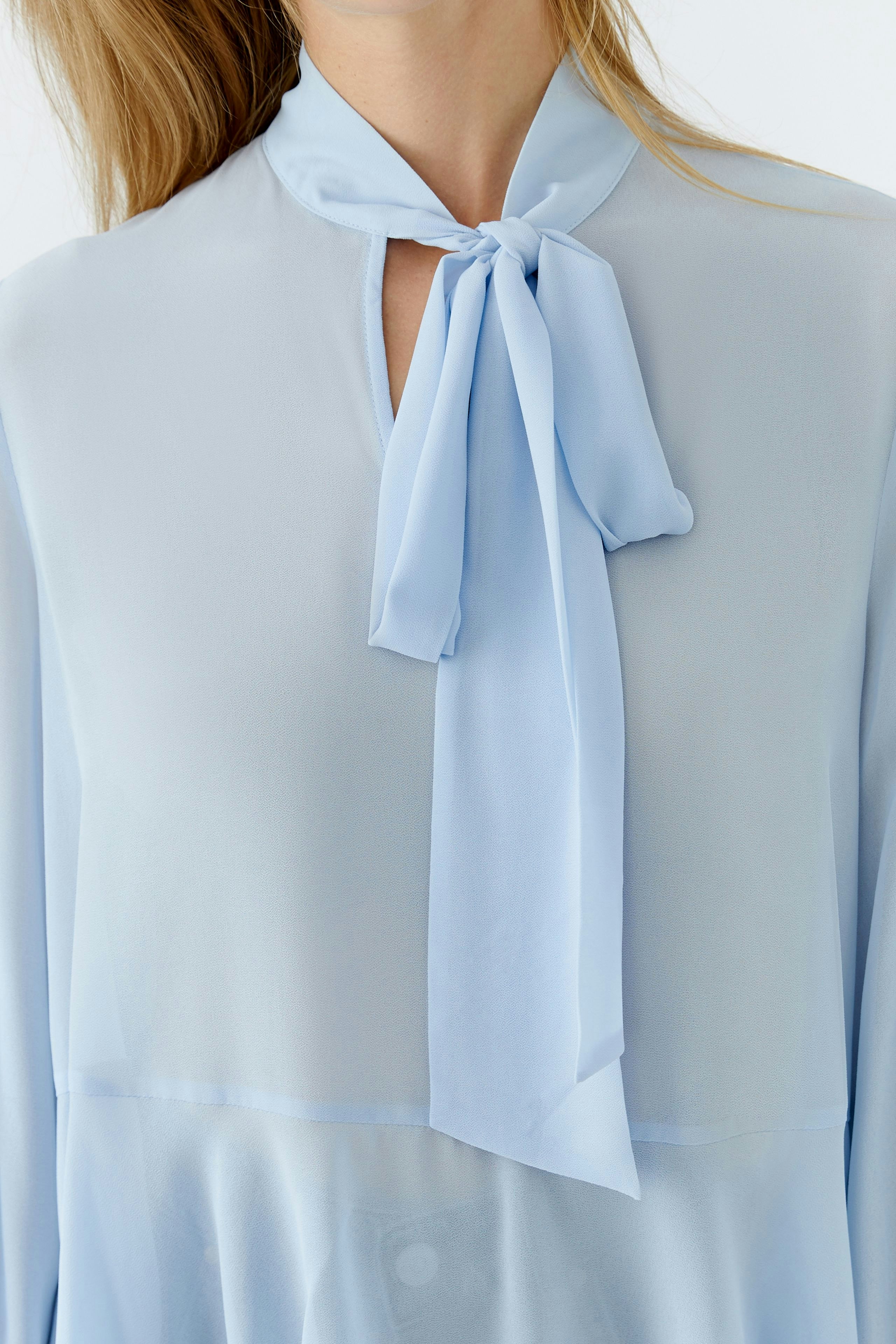 Light blue blouse with a tie detail, worn by a woman, offering a relaxed and stylish look.