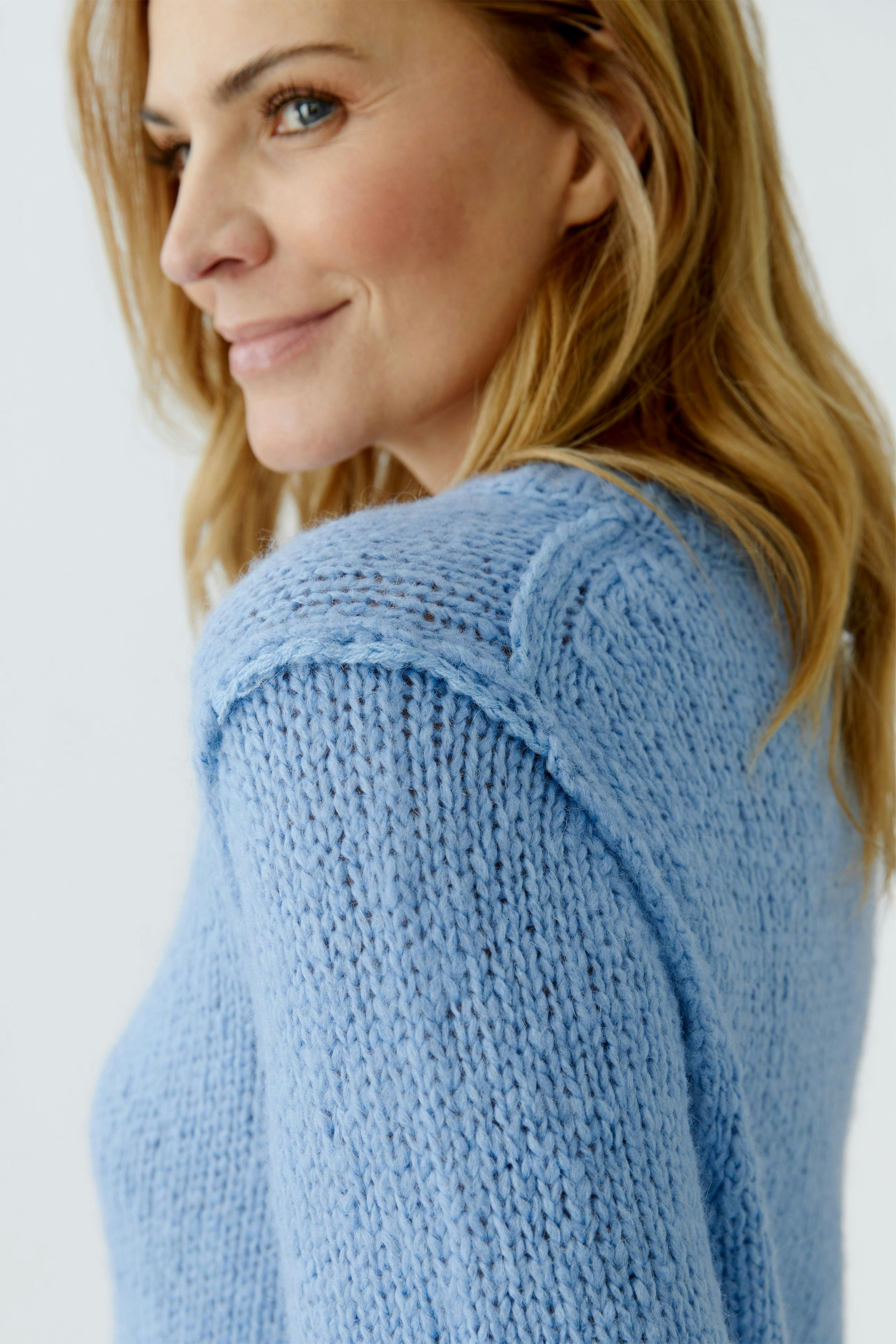 Damen-Pullover: Frau mit blauer Strickoptik, lässig und bequem, zeigt einen entspannten Look.