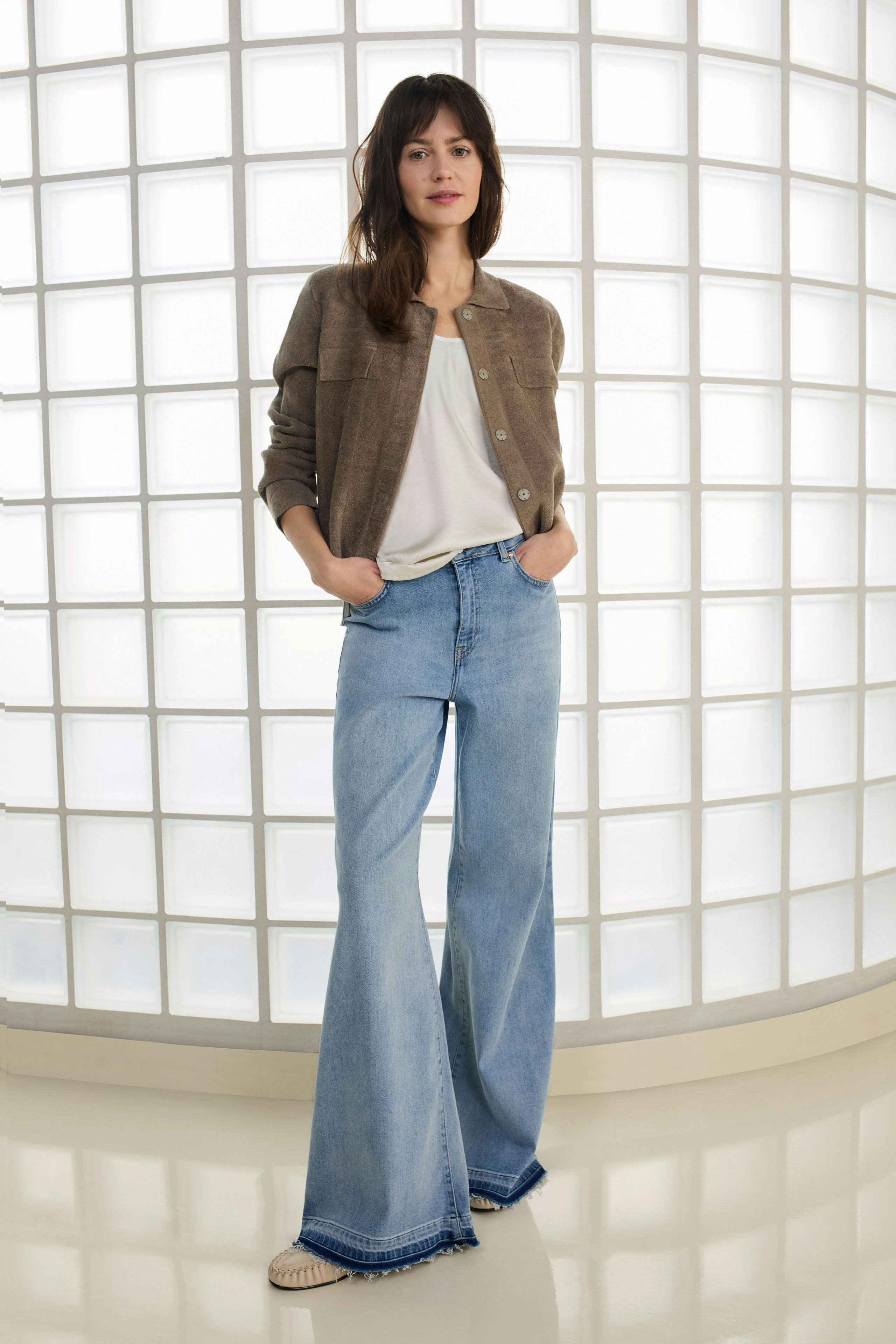 Casual women's flared jeans: Woman in light blue flared jeans and pink fluffy jacket poses on a soft surface.