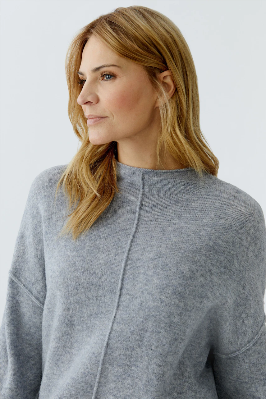 Casual women's pullover: Woman in a soft gray pullover with a relaxed fit, looking thoughtfully to the side.