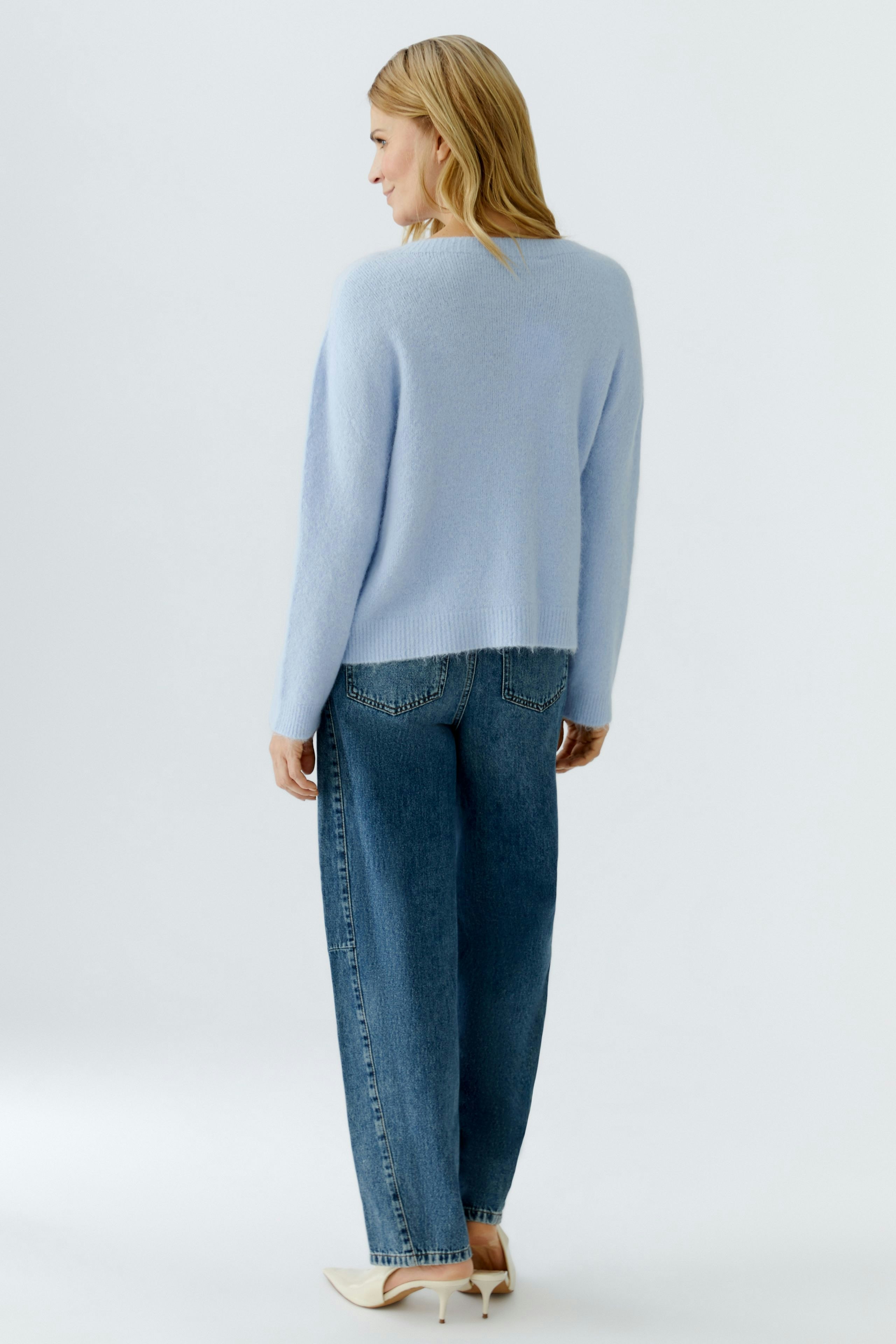 Casual women's pullover: A woman in a light blue pullover and relaxed jeans stands with her back to the camera.