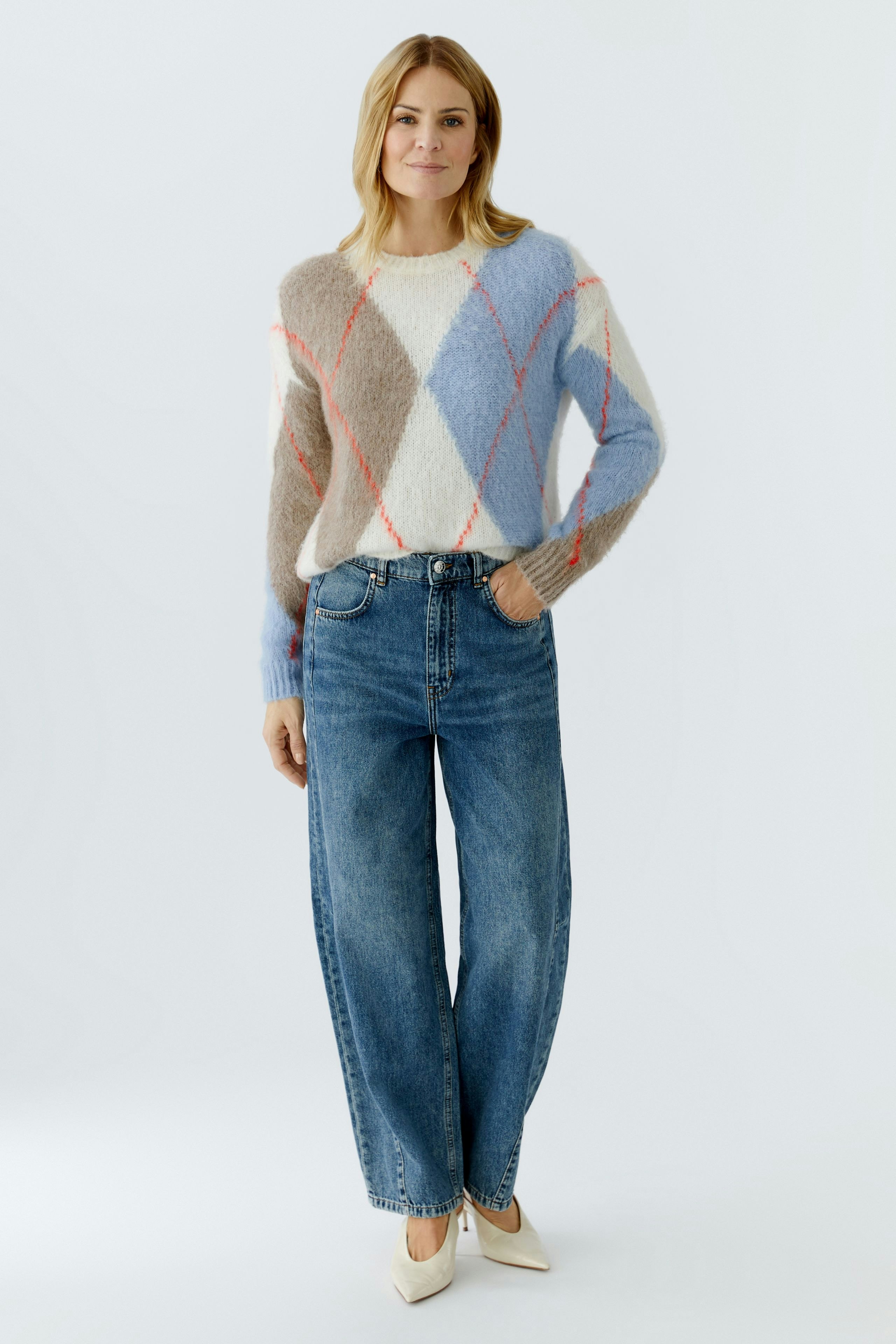 Casual women's pullover: A woman in a cozy, multicolored pullover with a diamond pattern and wide jeans.