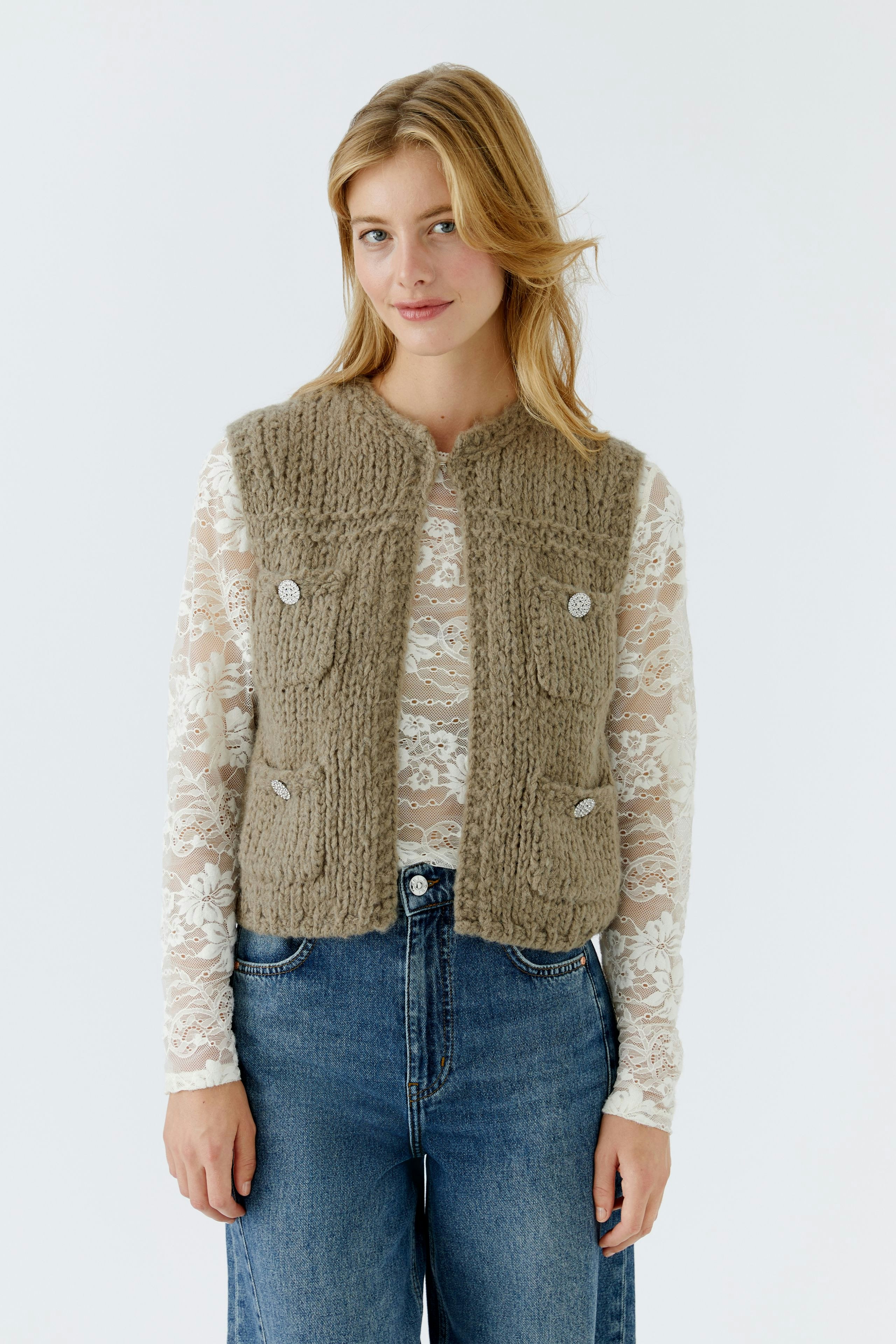 Beige Strickweste: Junge Frau trägt eine lässige Weste mit Knöpfen über einem Spitzenoberteil.