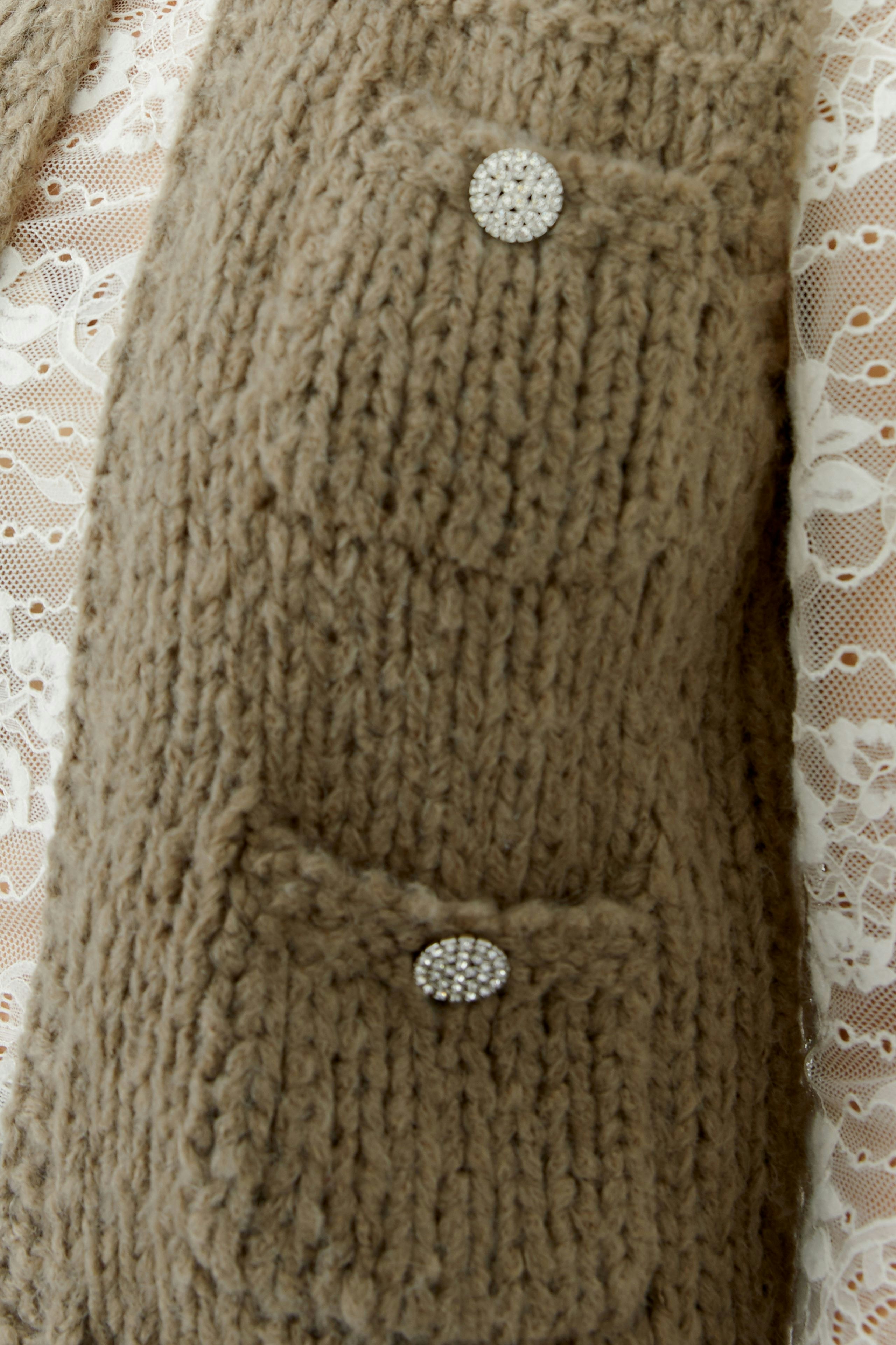 Beige Strickweste mit zwei Taschen und glitzernden Knöpfen, ideal für lässige Outfits.