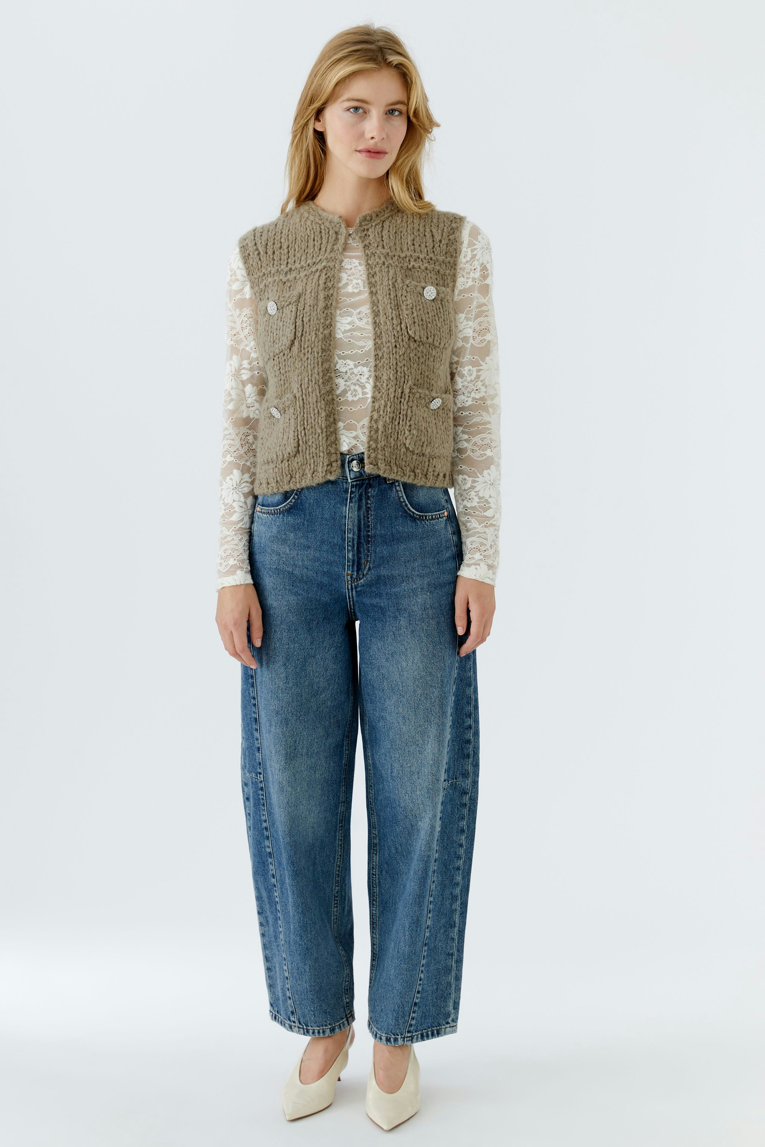Damen-Strickweste: Frau in beiger Weste mit Knöpfen, kombiniert mit lässiger Bluse und Jeans.