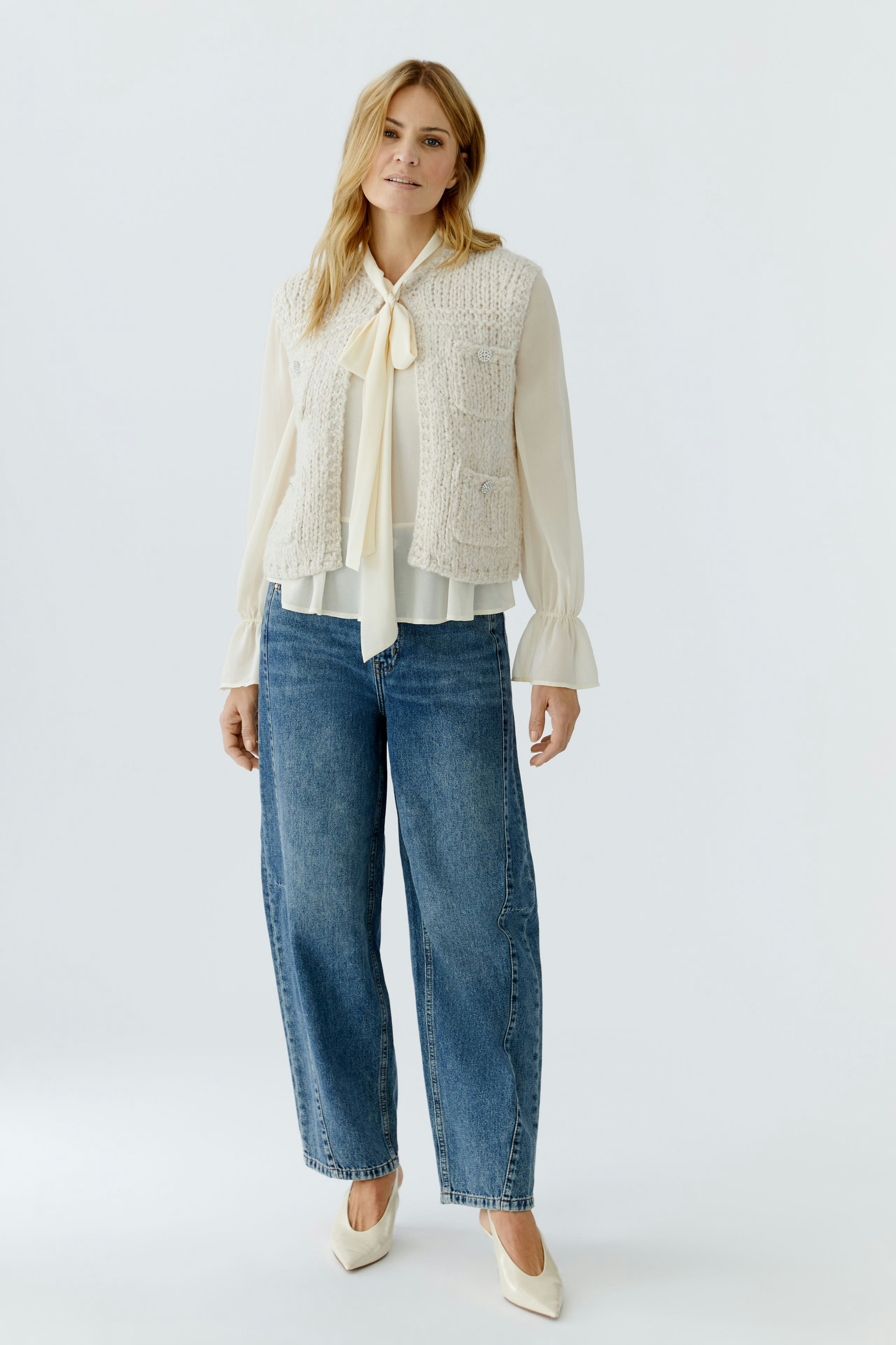 Beige Strickweste: Frau trägt eine lässige Strickweste über einer Bluse und Jeans.