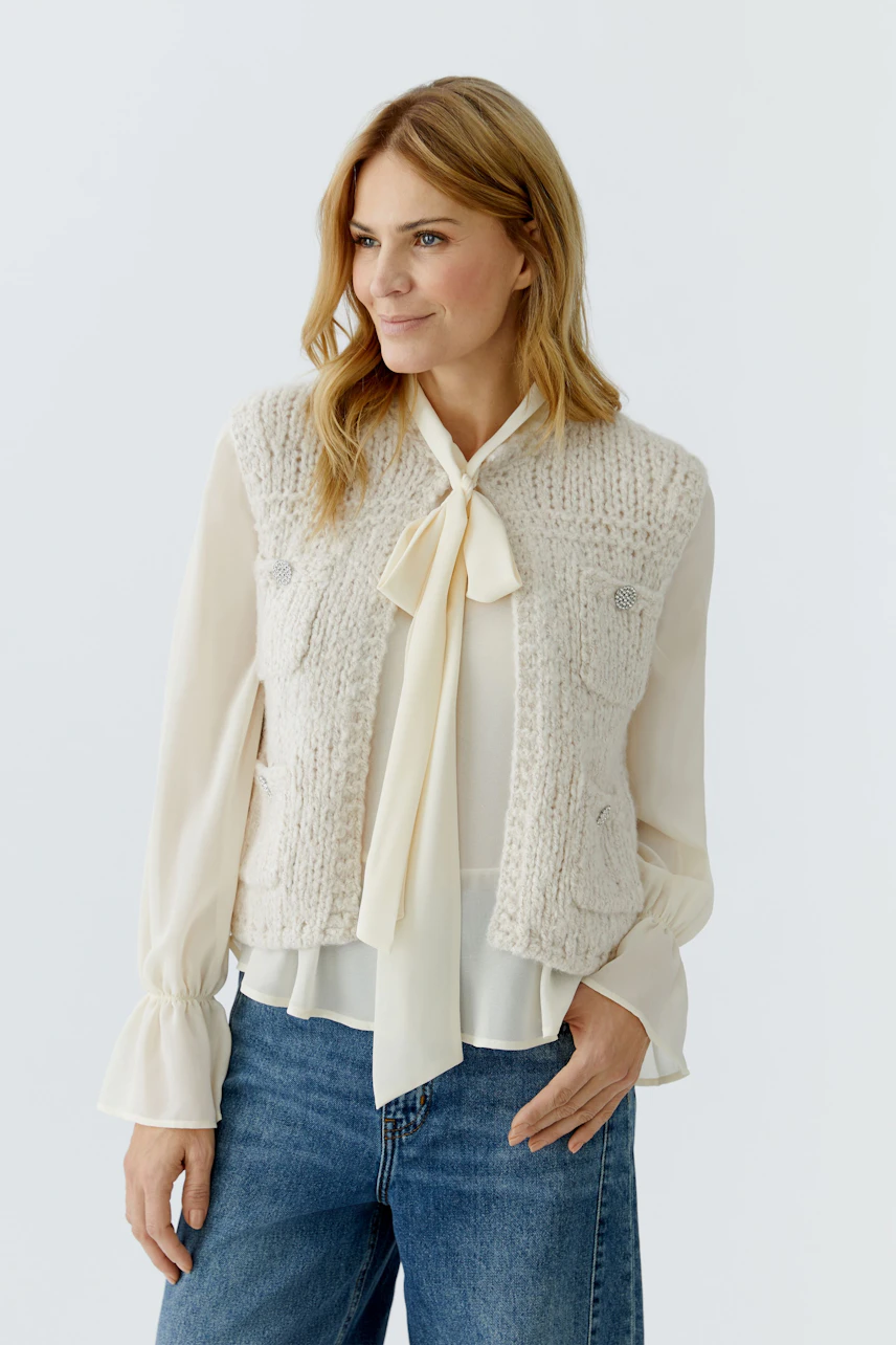 Casual women's cardigan: Woman in a light knitted vest over a blouse, paired with jeans.