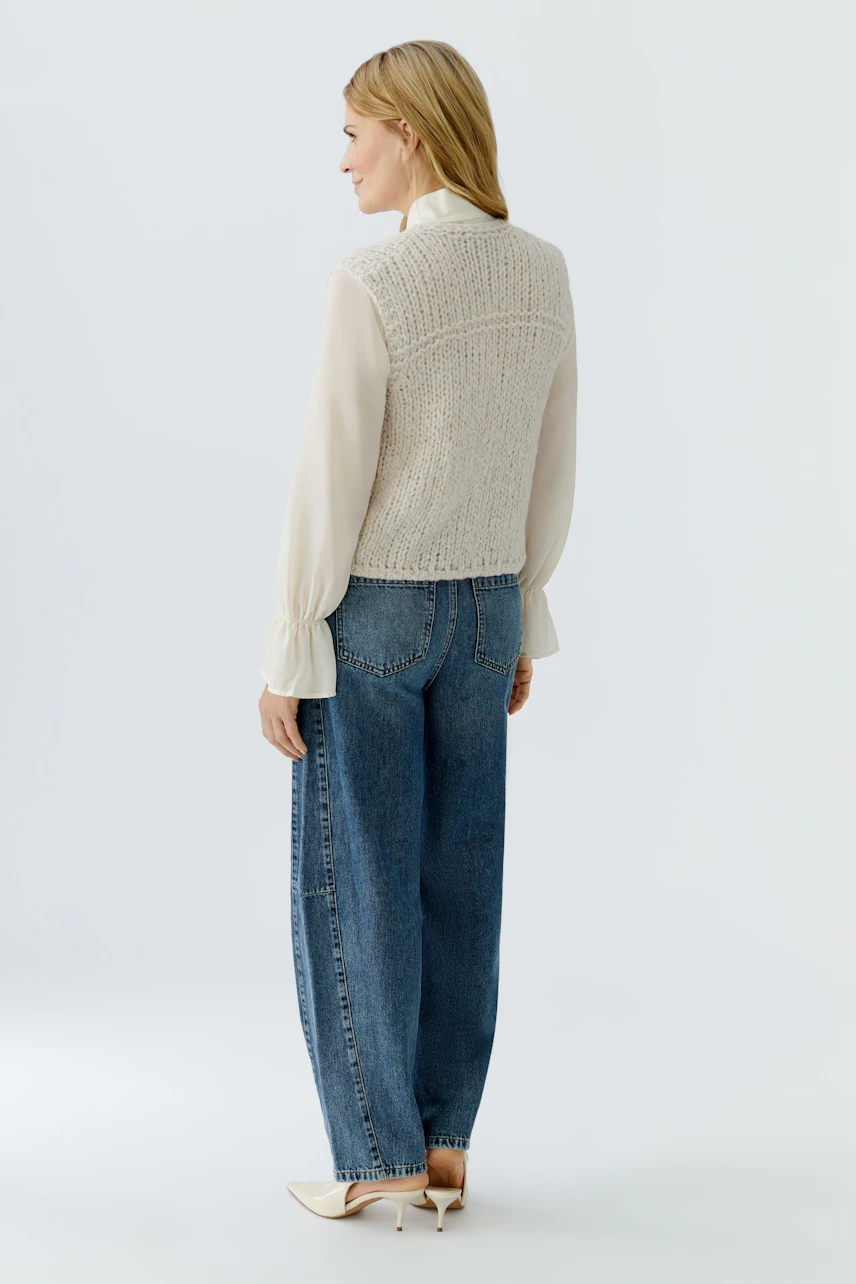 Casual women's knitted vest: A woman in a light knitted vest over a blouse and relaxed jeans.