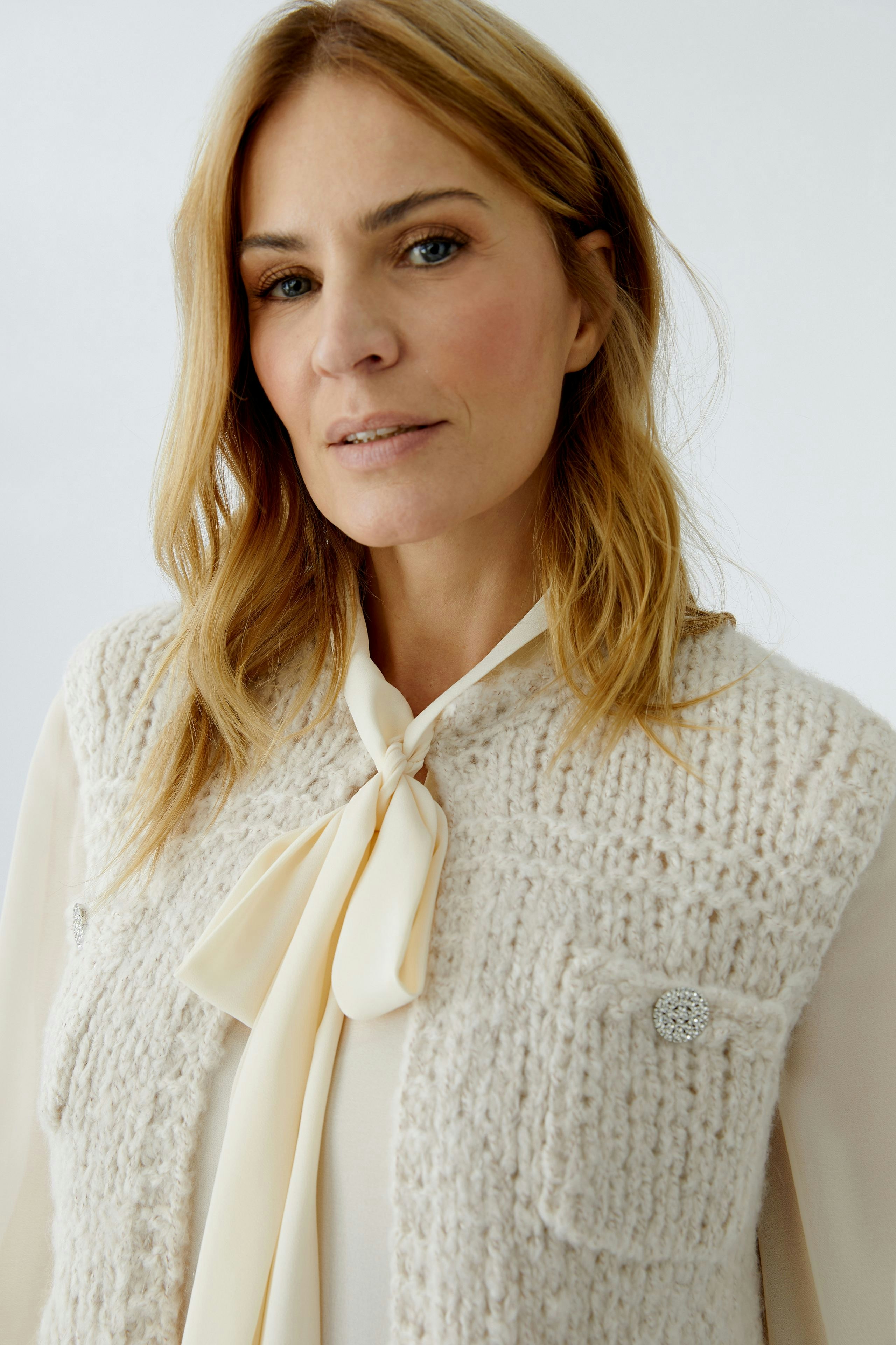 Beige Strickweste: Frau mit blonden Haaren trägt eine lässige, offene Strickweste mit Taschen.