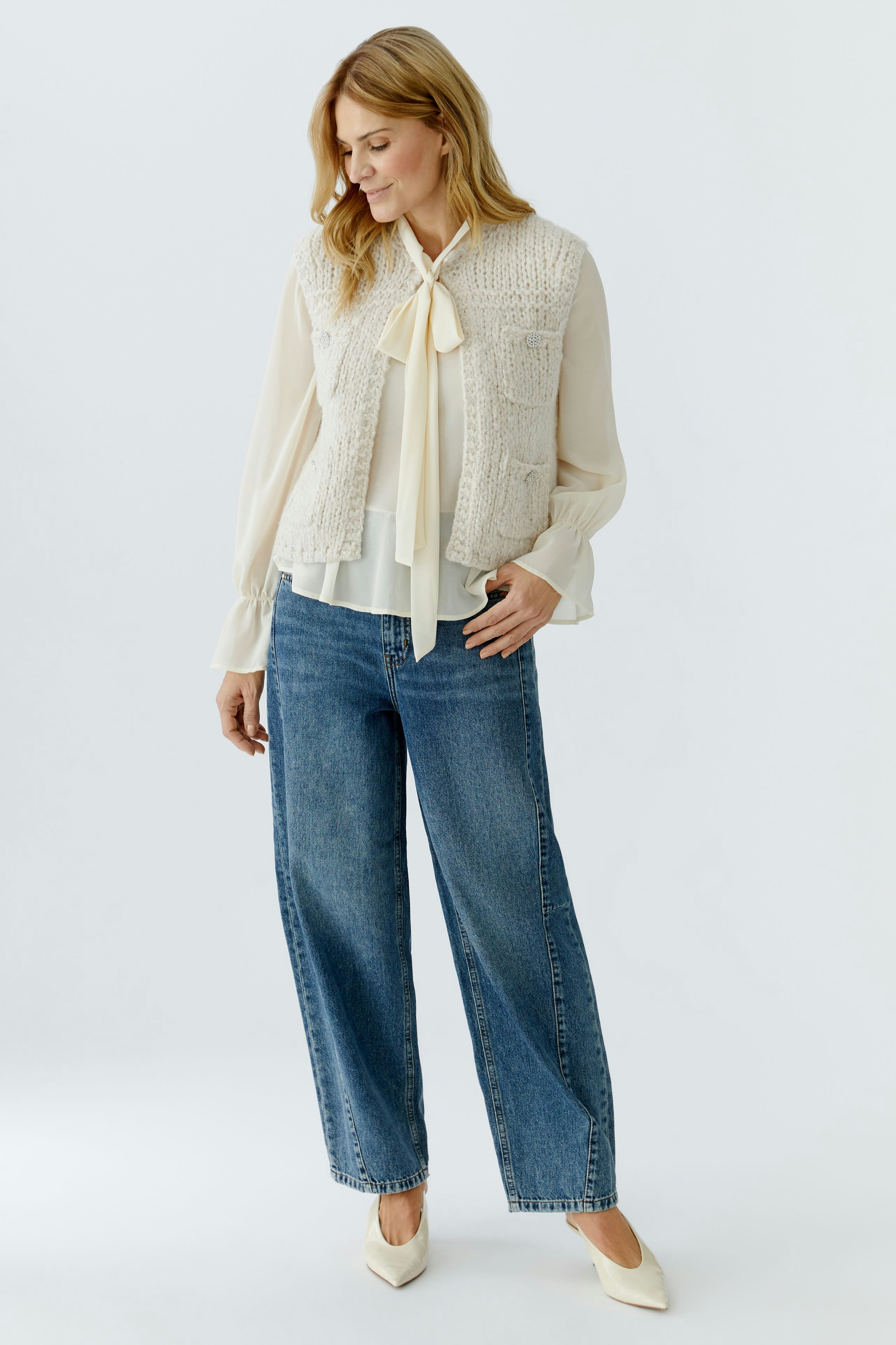 Damen-Strickweste: Frau in beiger Strickweste über bluse und Jeans, lässiger Look.