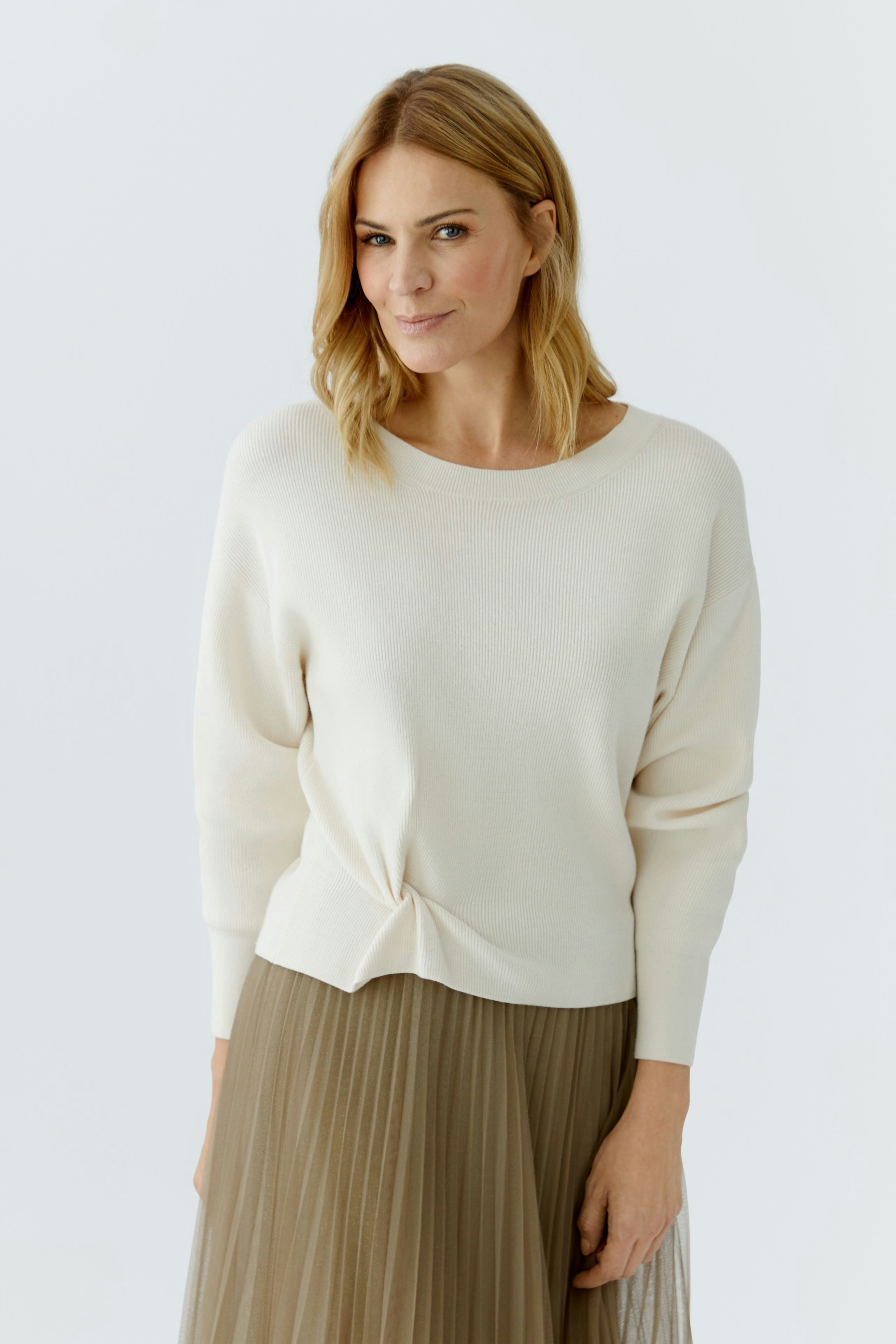 Casual women's pullover: A woman in a light cream pullover with a knotted front, paired with a flowy skirt.
