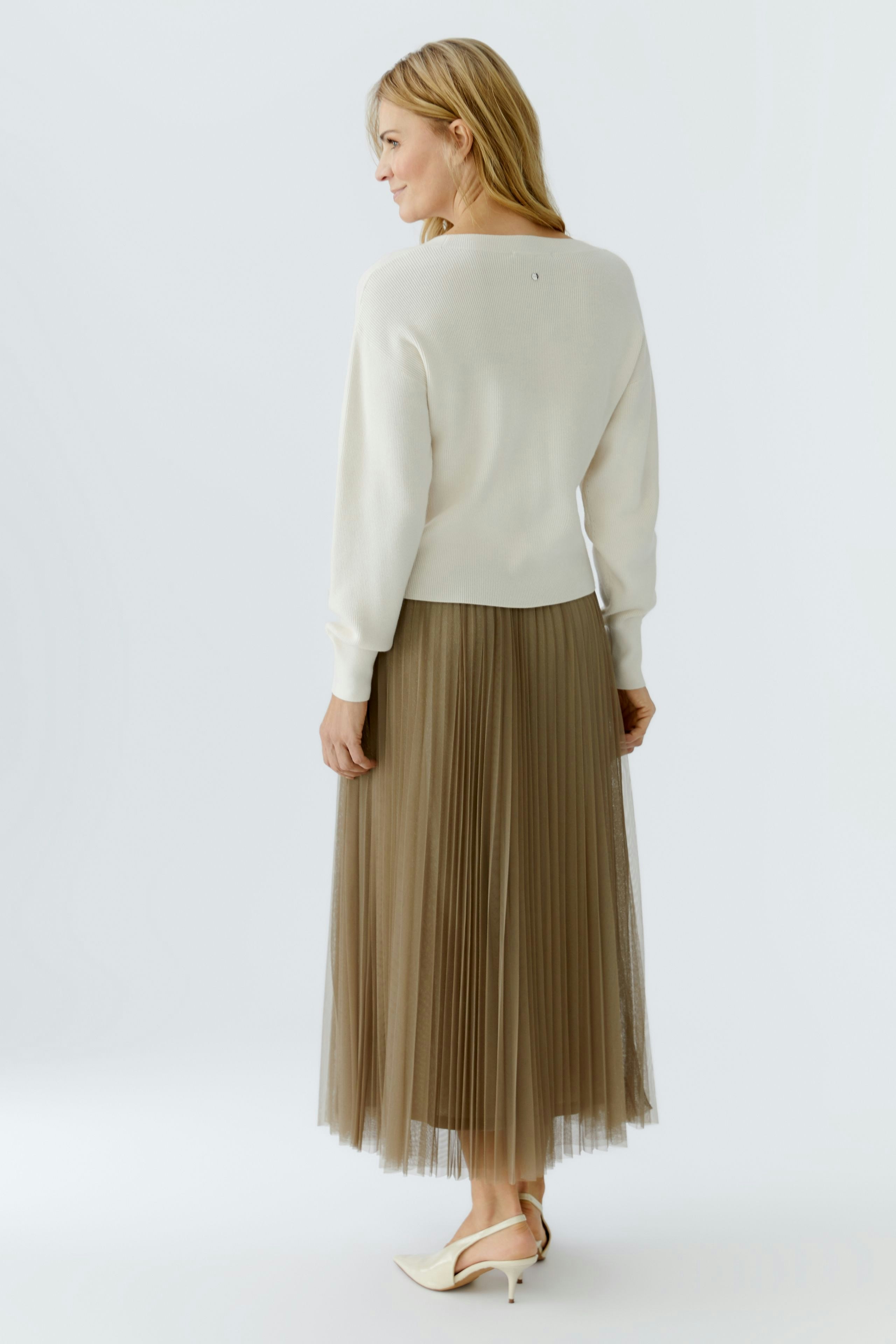 Casual women's pullover: A woman in a cream pullover paired with a pleated skirt, showcasing a relaxed style.