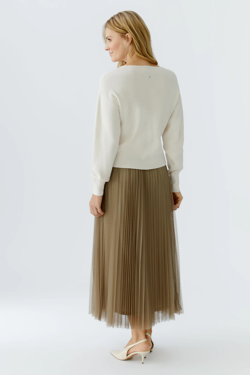 Casual women's pullover: A woman in a cream pullover paired with a pleated skirt, showcasing a relaxed style.